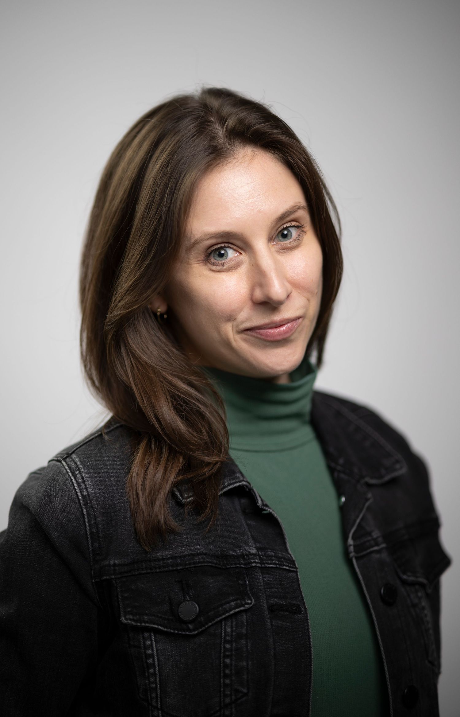Brunette woman with blue eyes in a green turtleneck and denim jacket in a professional portrait.