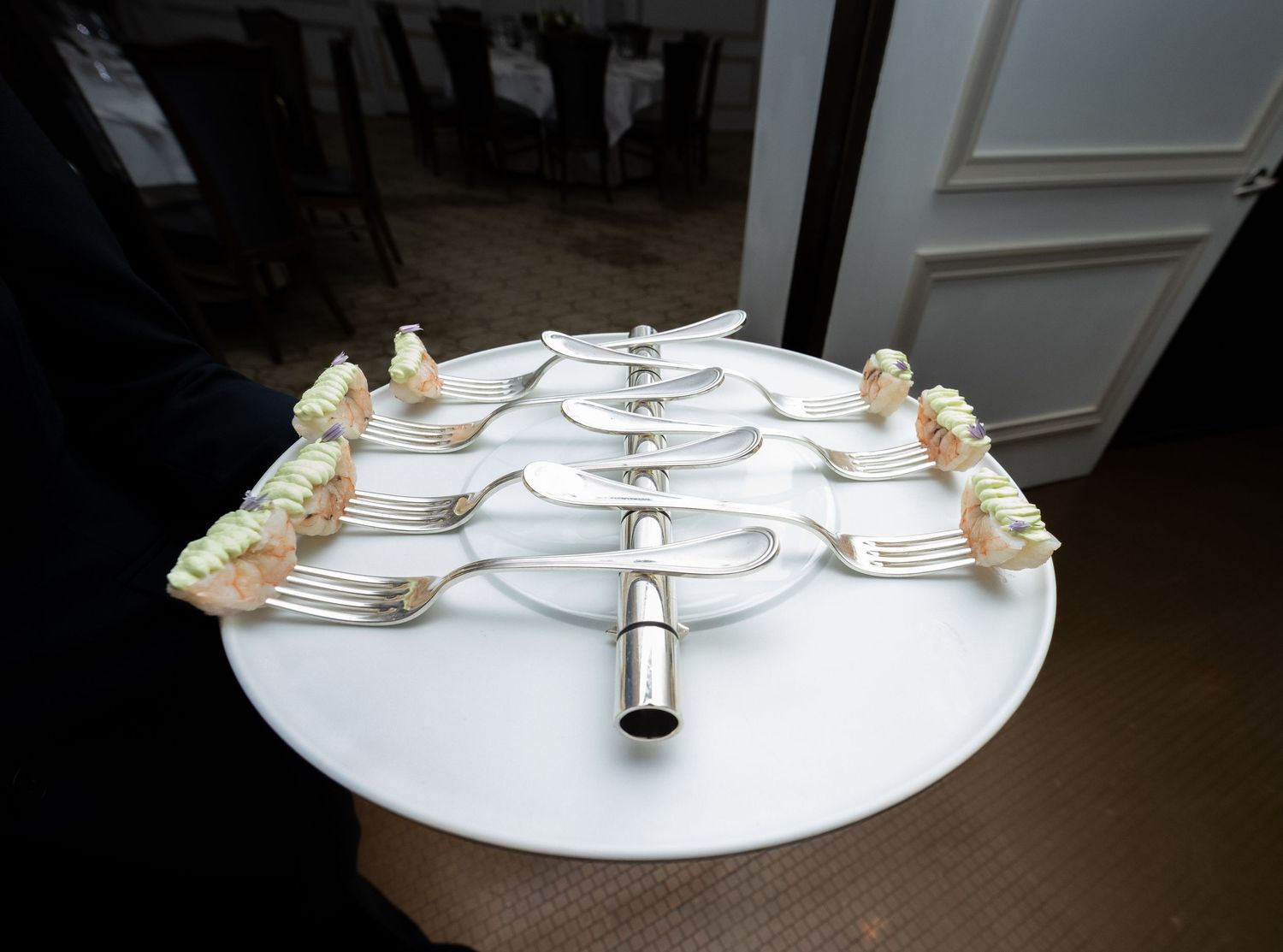 Creative wedding catering display with silver forks fanned out holding floral appetizers on a round table.