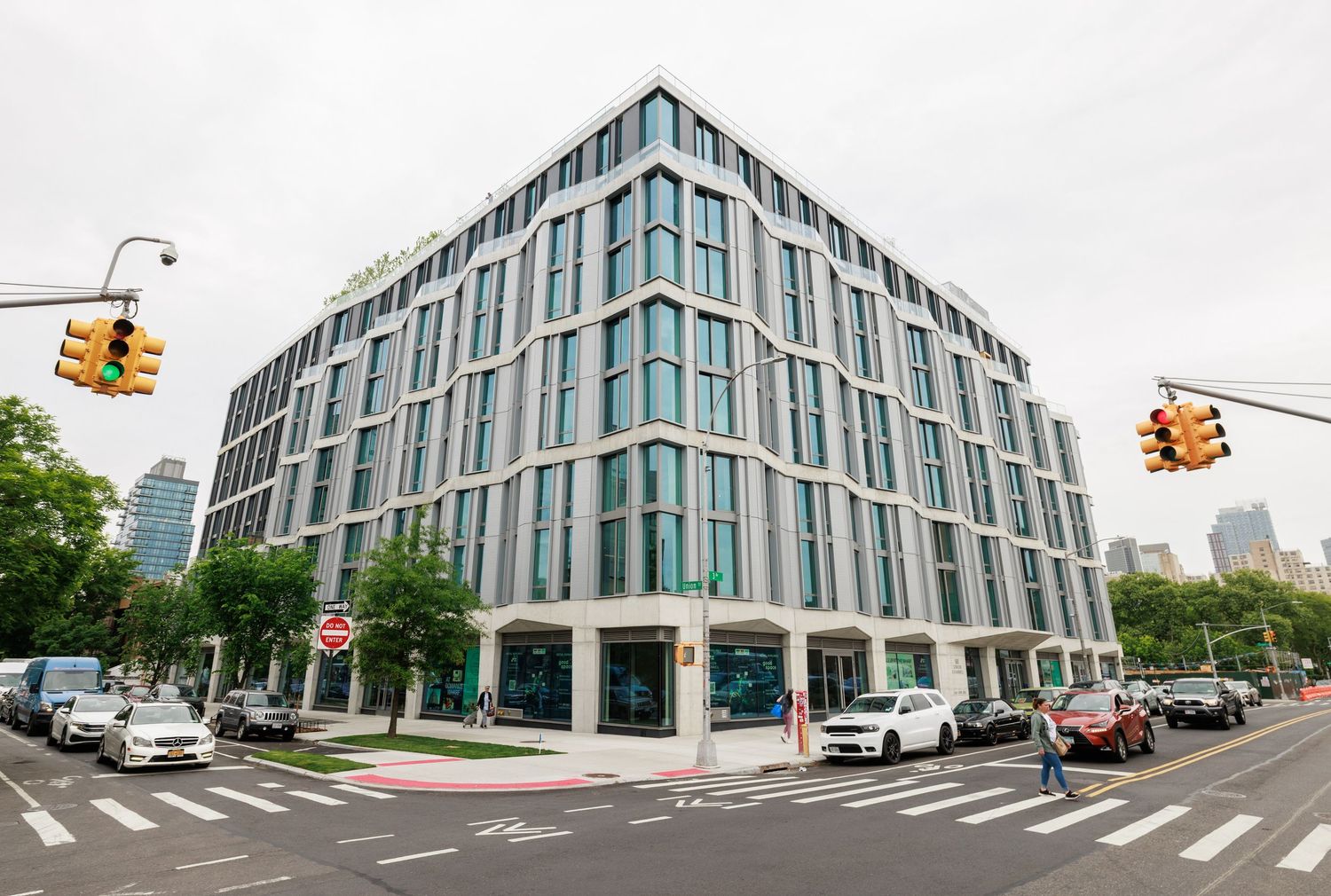 Modern glass and steel corner apartment building at a busy urban intersection with traffic lights.