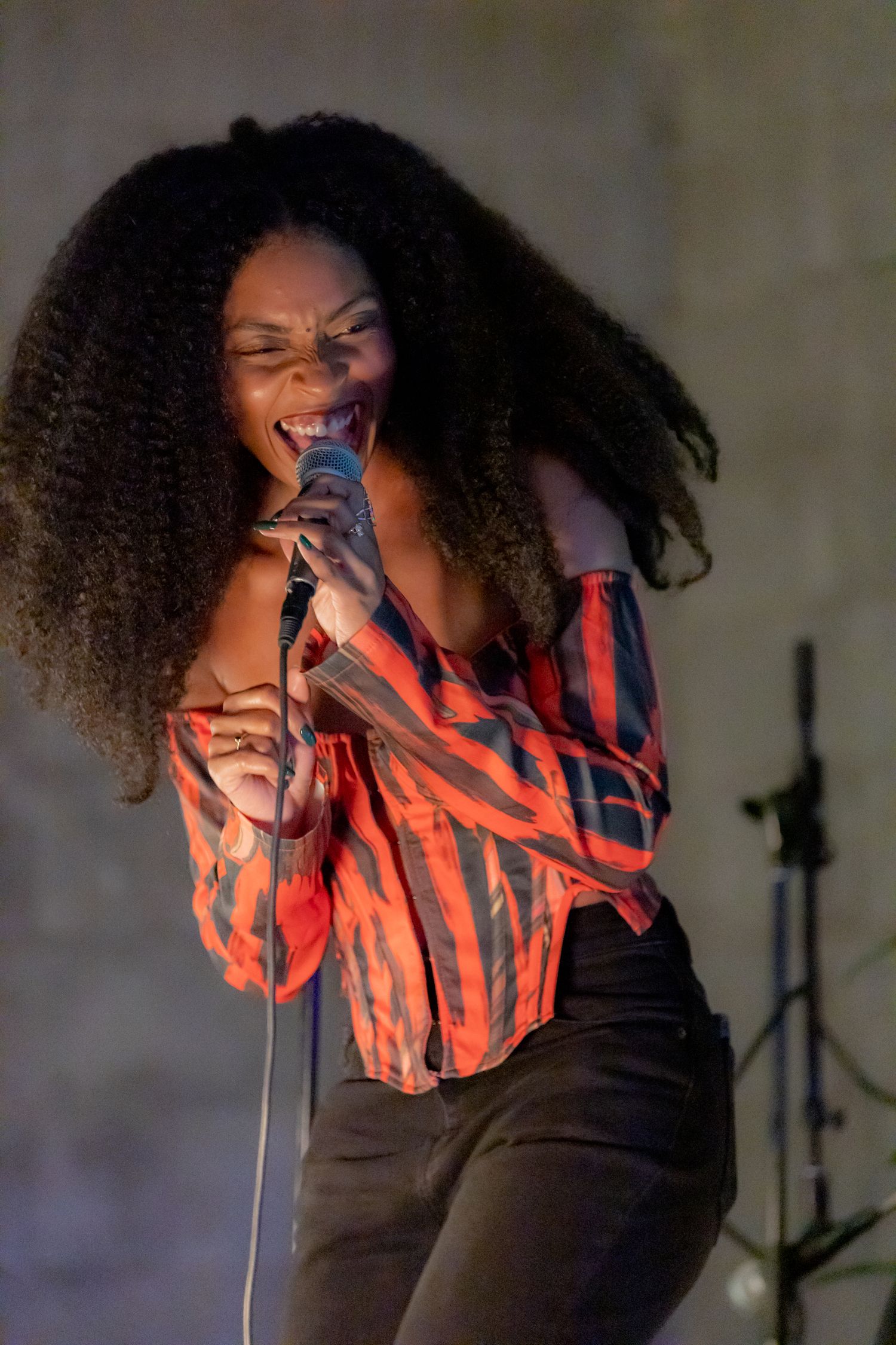Passionate female singer performing on stage with microphone and curly hair flowing.