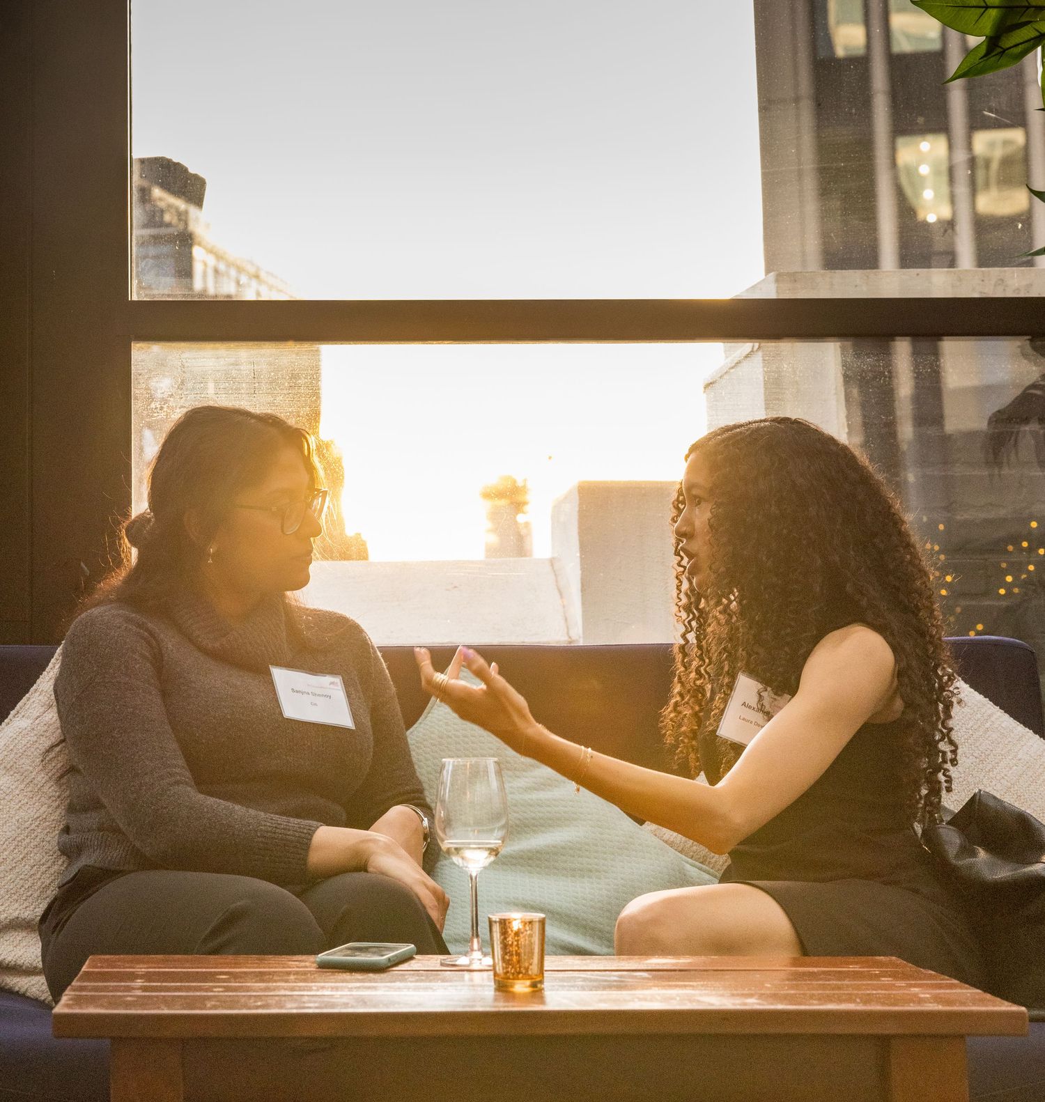 Two women having an intimate conversation at a networking event with city skyline at sunset.