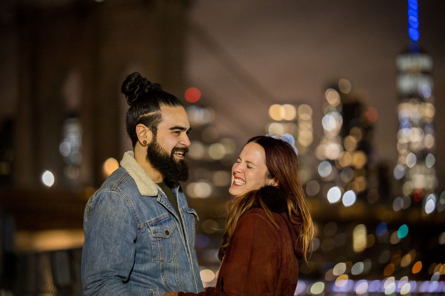 Happy couple laughing together at night with New York City skyline bokeh lights behind them.