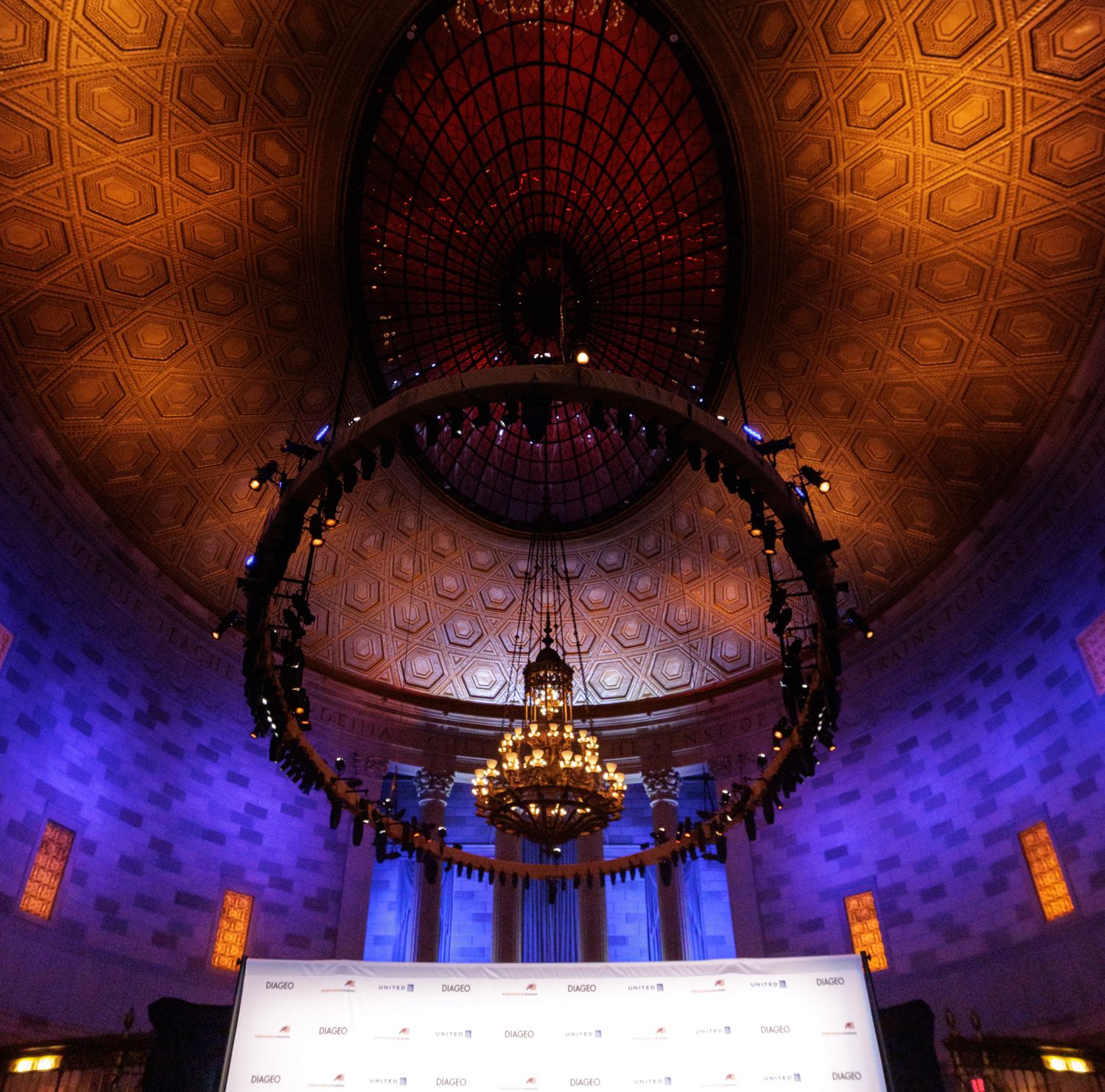 Grand event hall with ornate golden ceiling, dramatic chandelier, and purple ambient lighting.