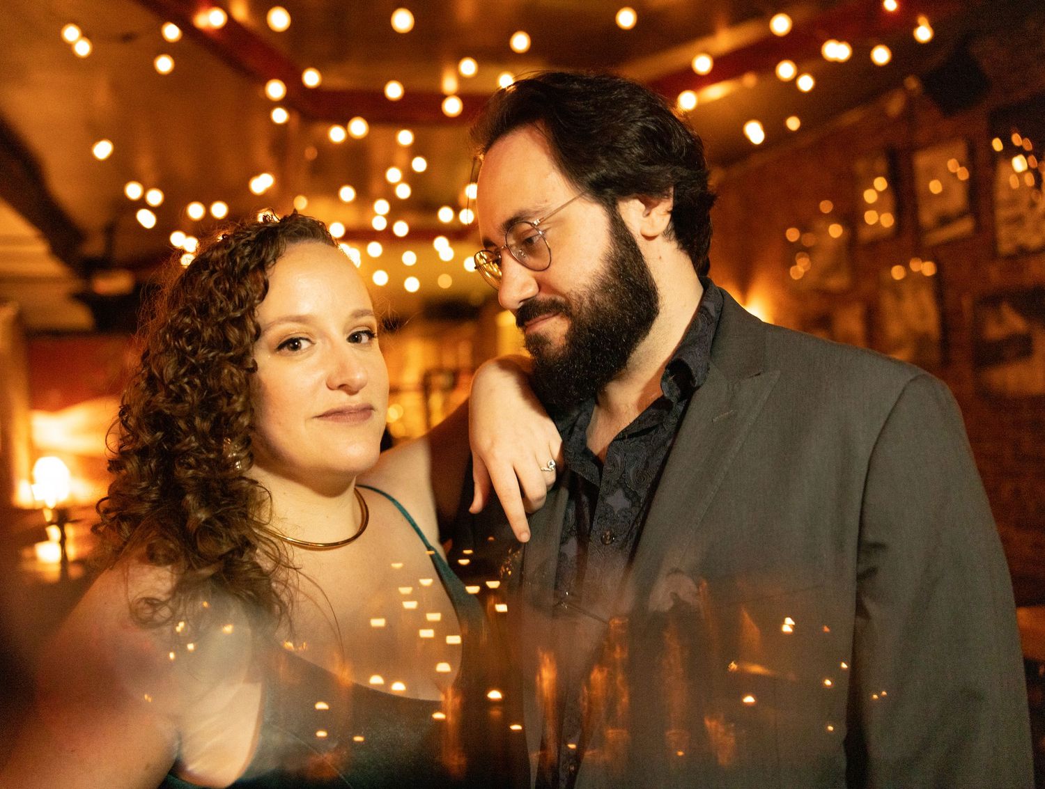 Romantic couple sharing an intimate moment surrounded by warm bokeh string lights indoors.