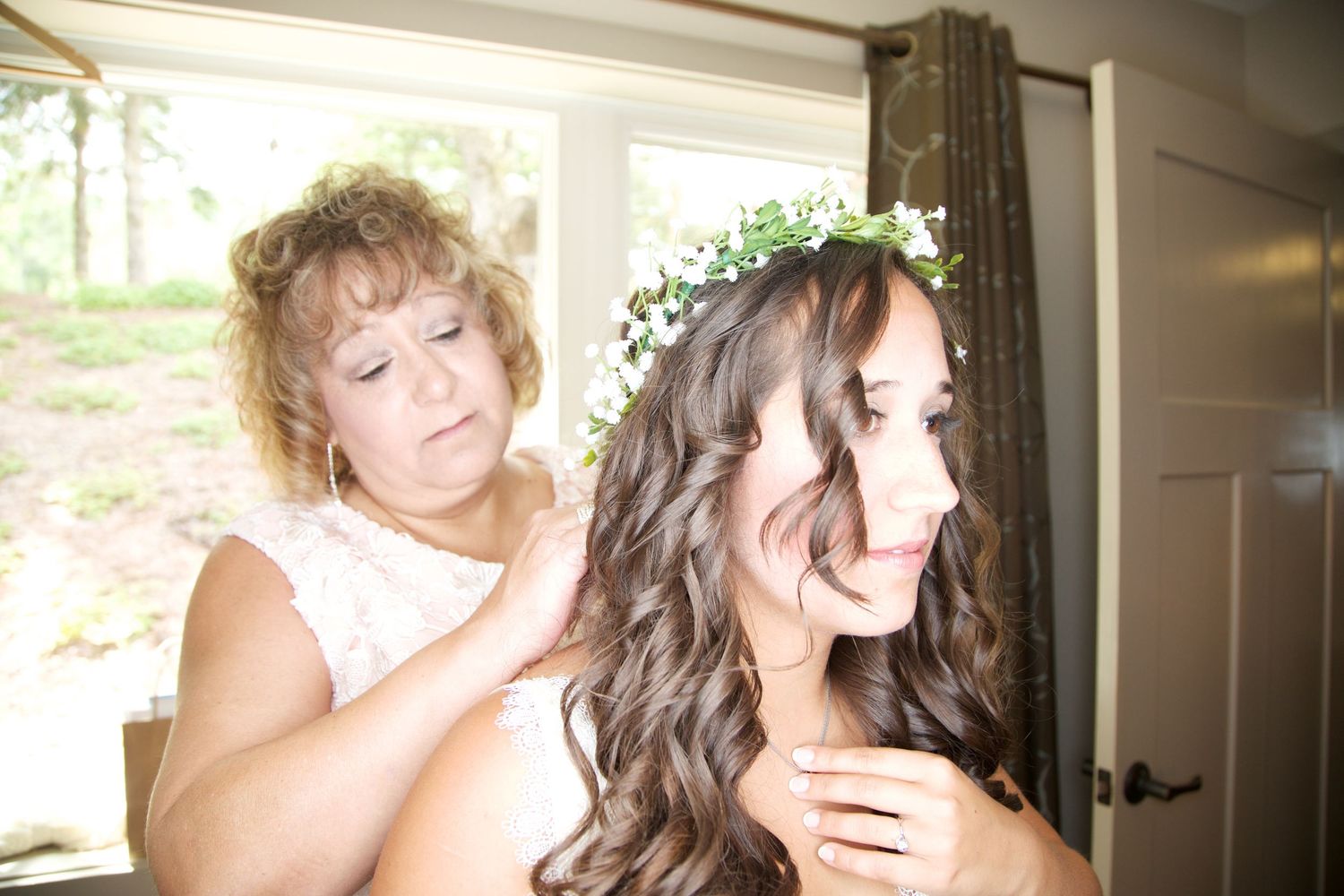 Mother carefully adjusts a floral crown in brides dark curly hair during wedding preparations.