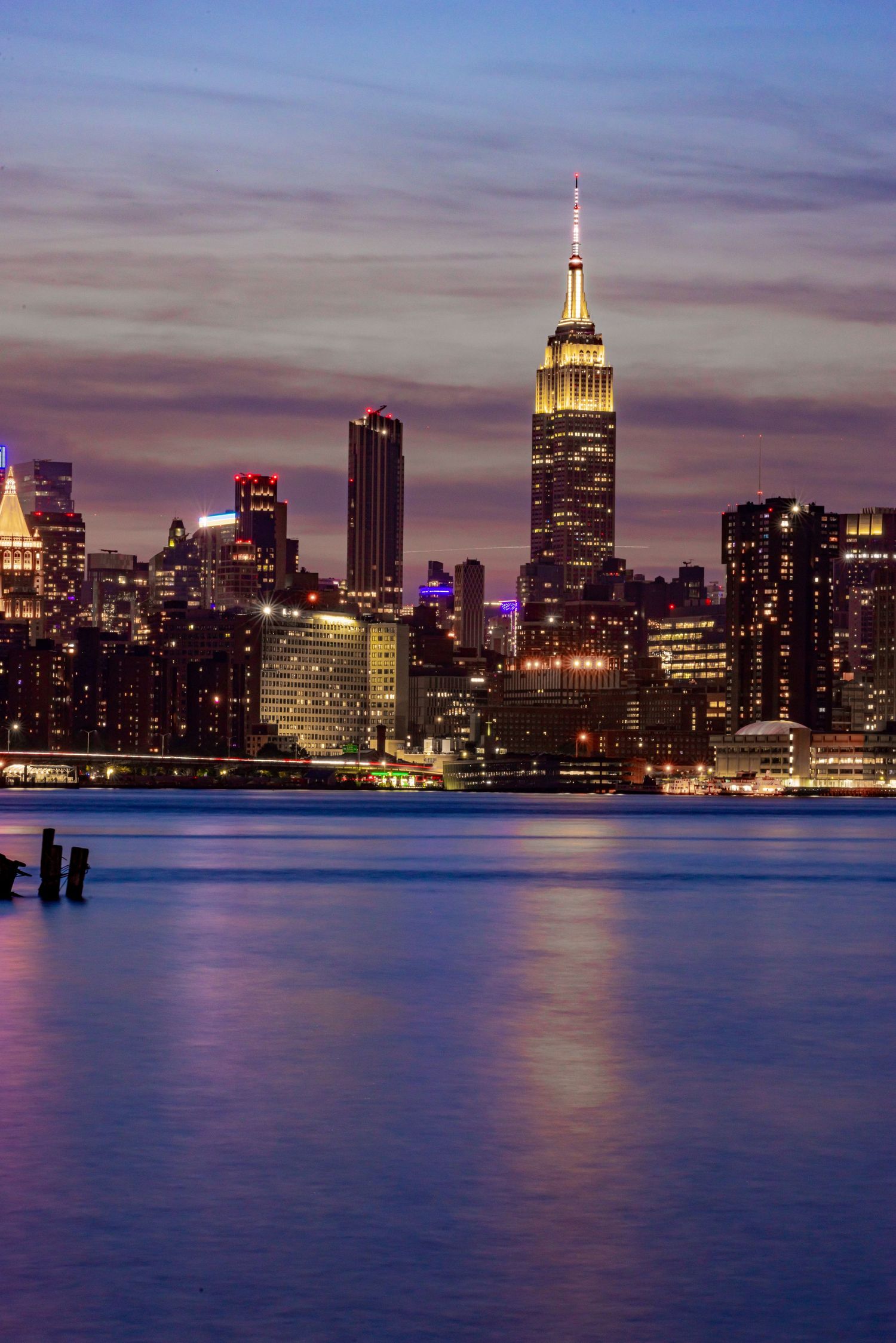 New York City skyline at dusk featuring Empire State Building reflected in Hudson River.