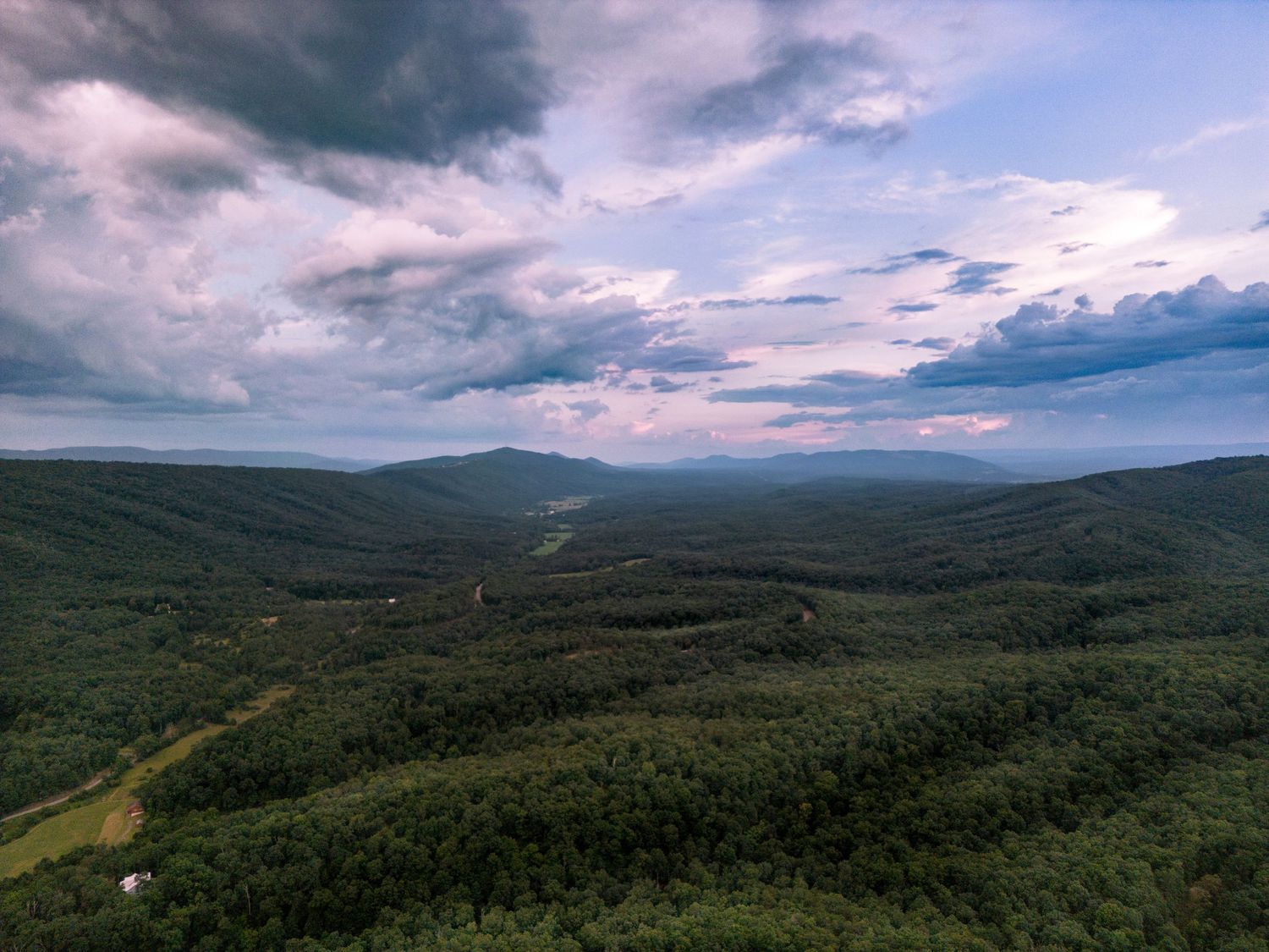 Aerial view of lush green rolling mountain valleys under dramatic cloudy sky at dusk.