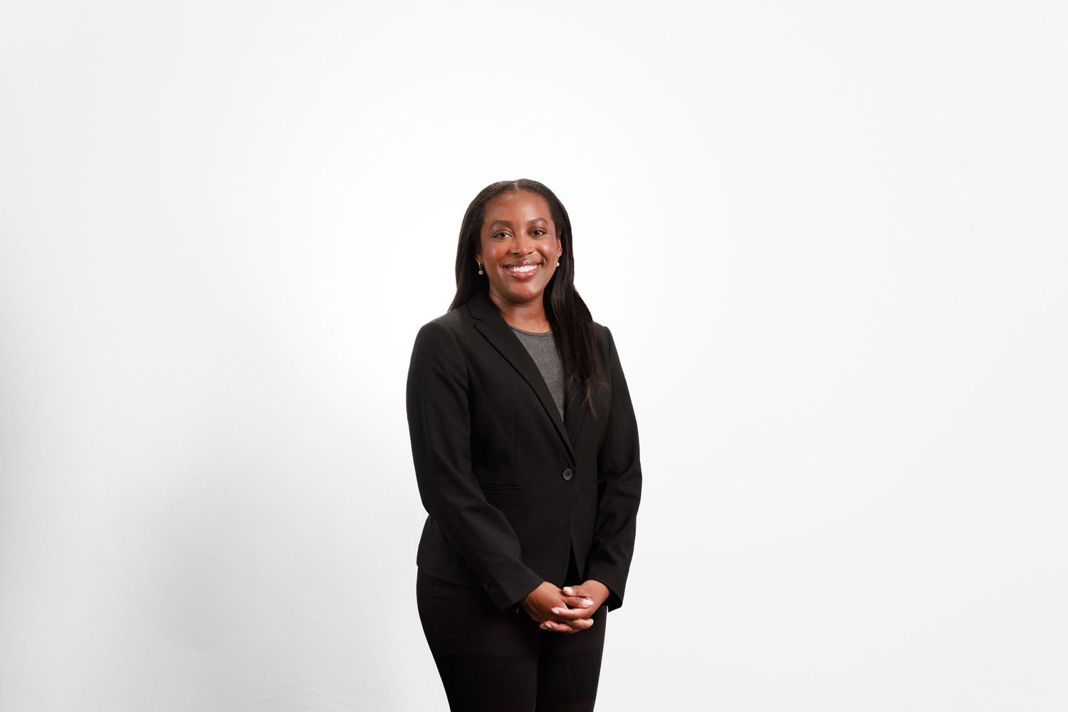 Professional woman in black blazer smiling confidently against a clean white studio background.