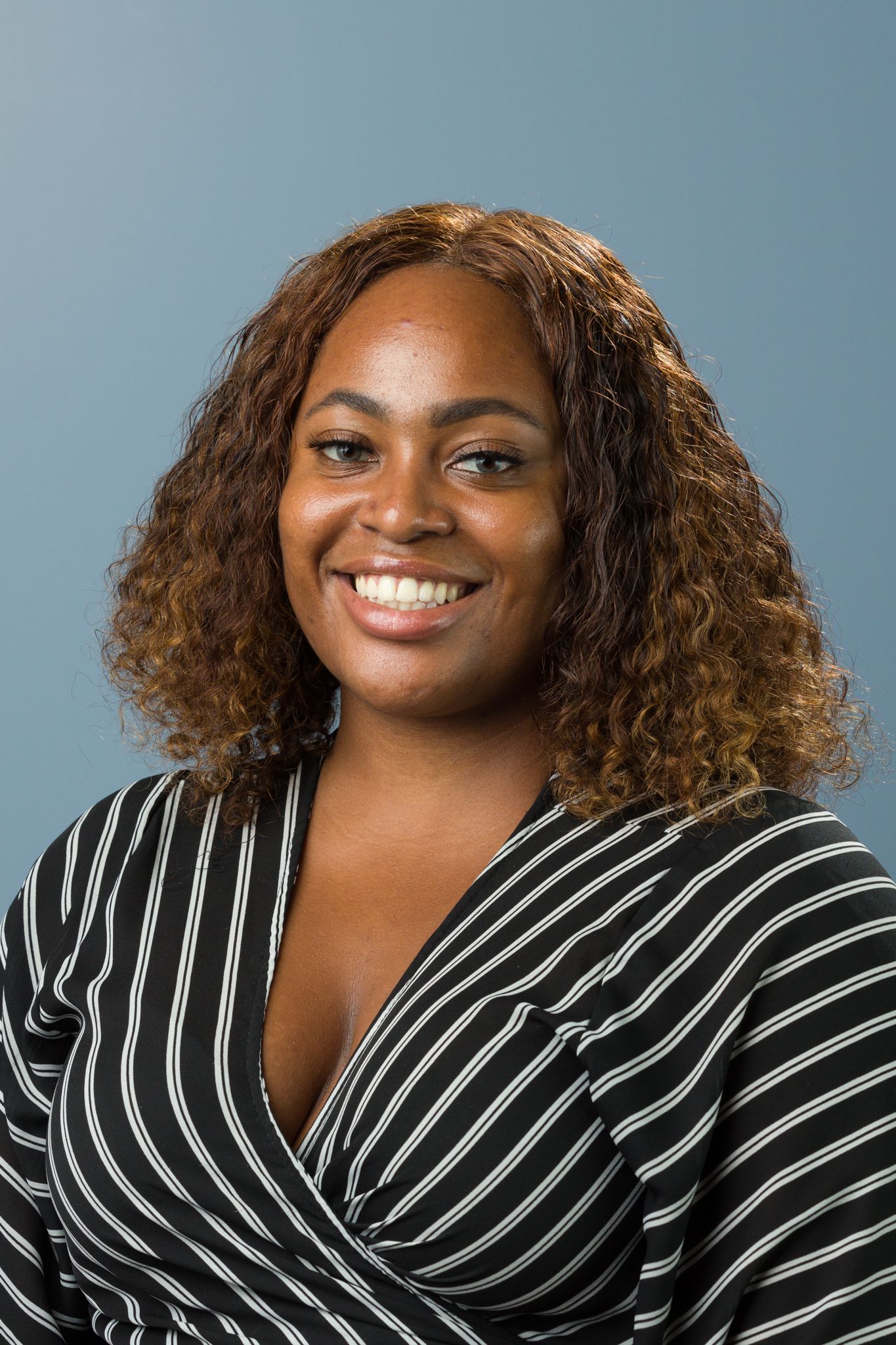Smiling woman with curly brown hair wearing a striped wrap top in a professional headshot.