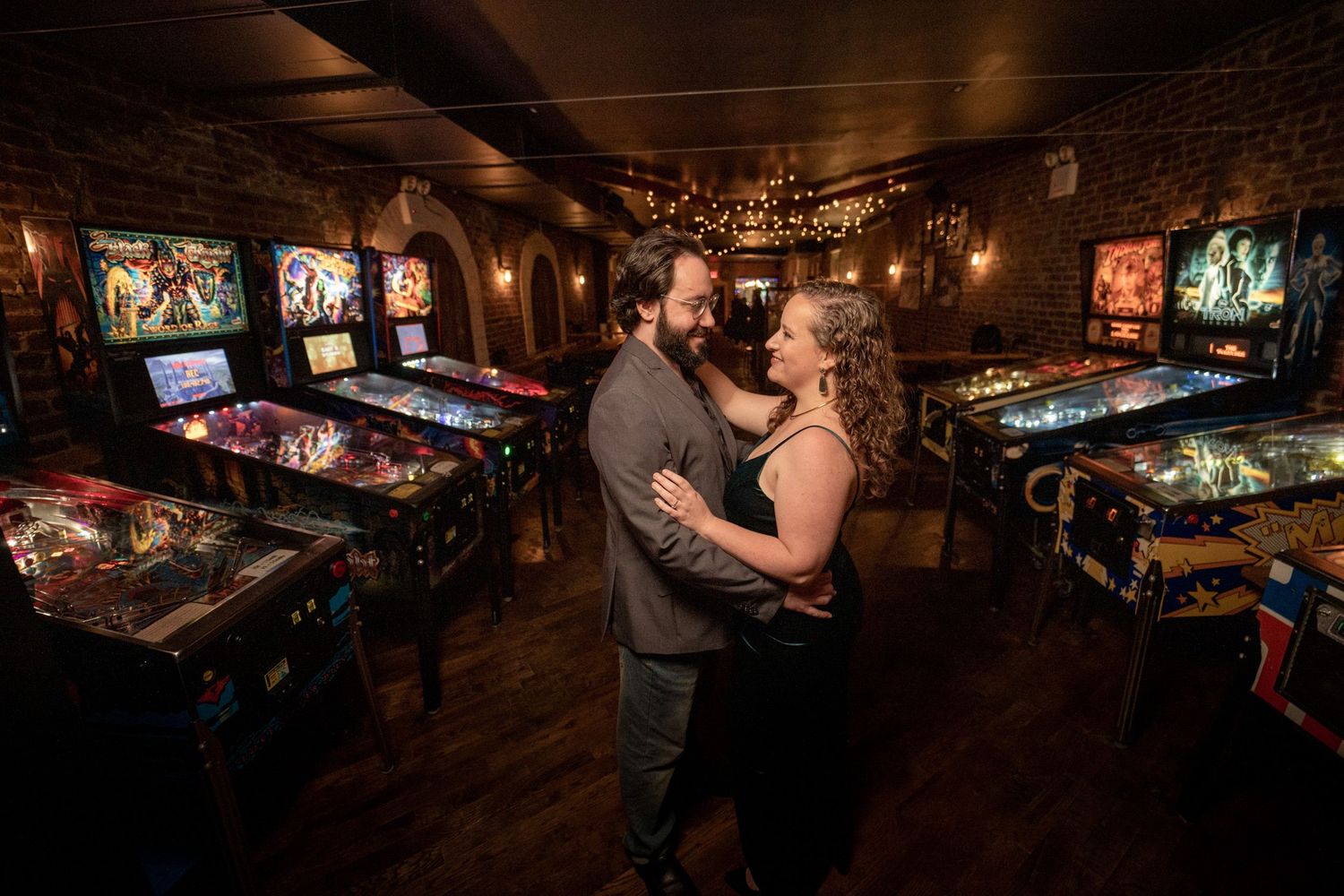 Couple embracing romantically in a vintage arcade room surrounded by pinball machines.