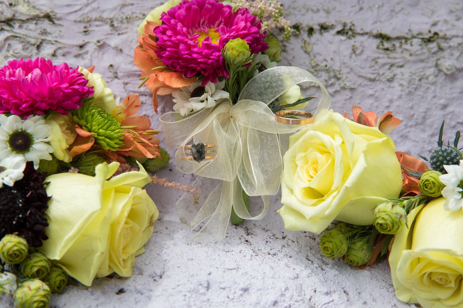 Colorful wedding boutonnieres and floral arrangements with yellow roses and pink blooms.