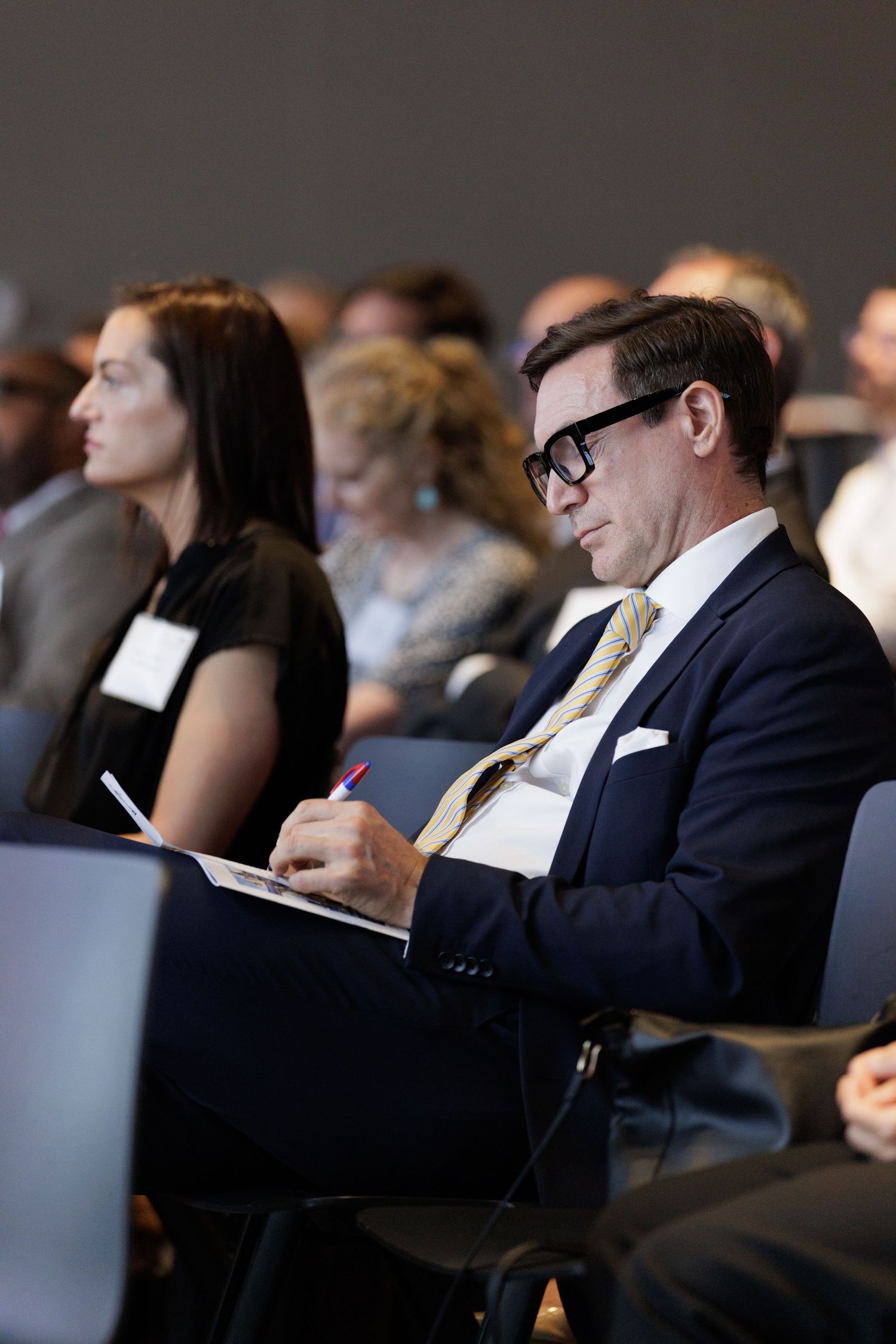 Businessman in suit taking notes on a clipboard while attending a professional conference or seminar.