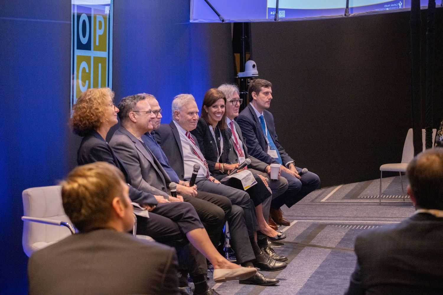 Panel of seven professionals seated on stage during a discussion at an Open City conference event.