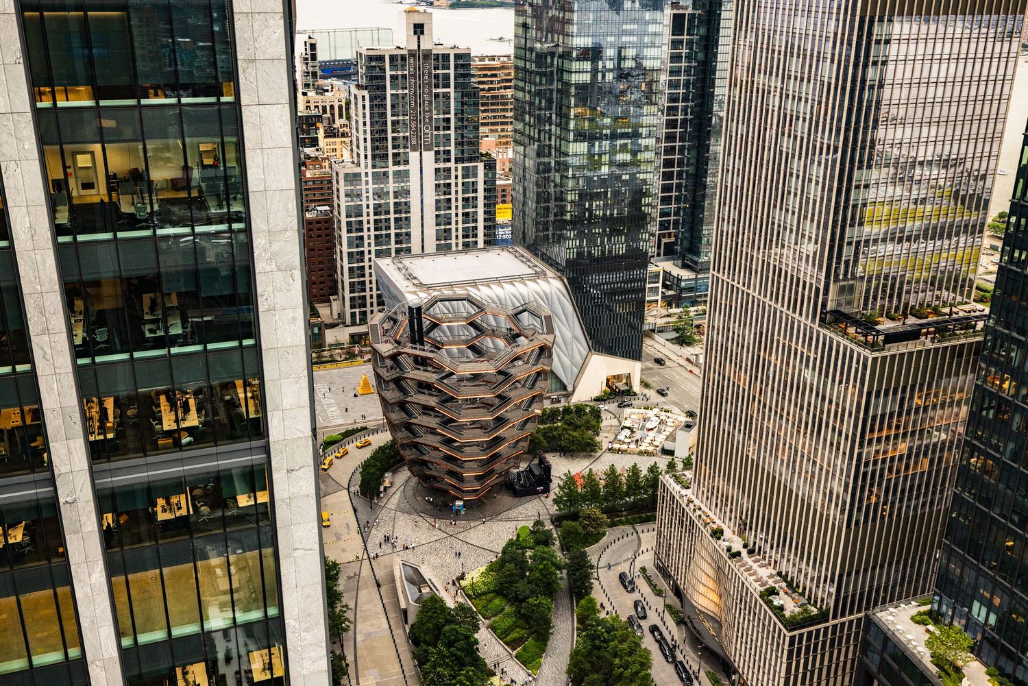Aerial view of the Vessel honeycomb structure at Hudson Yards surrounded by modern glass skyscrapers in New York City.