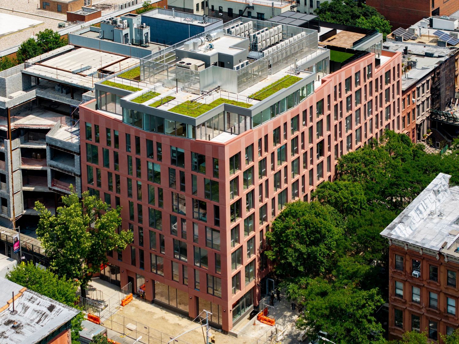 Aerial view of a red brick residential apartment building with rooftop garden in an urban neighborhood.