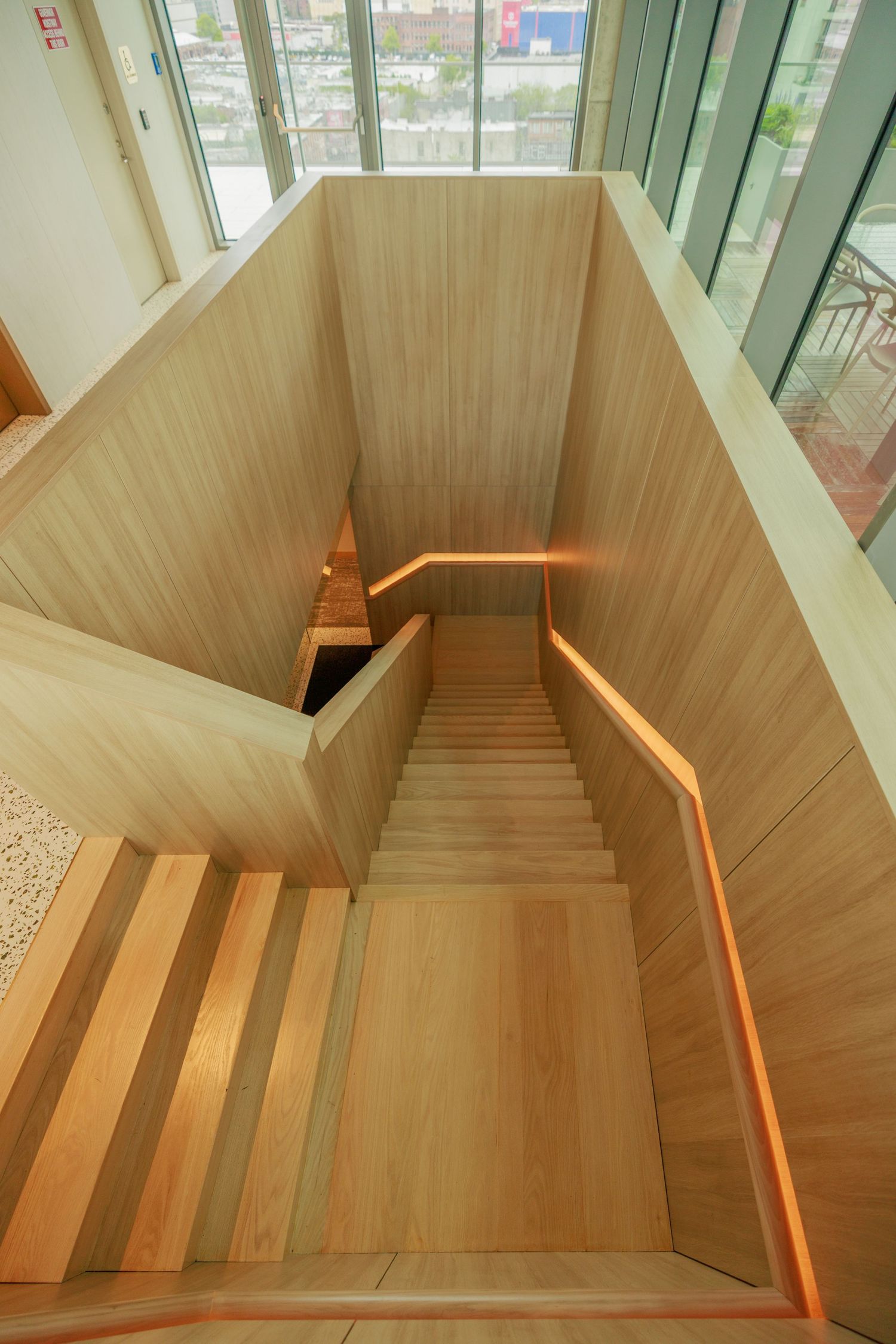 Modern wooden staircase with warm LED strip lighting viewed from above in a contemporary building interior.