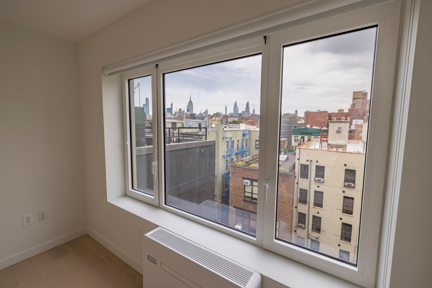 Large triple-pane window offering panoramic views of New York City rooftops and skyline from an apartment.