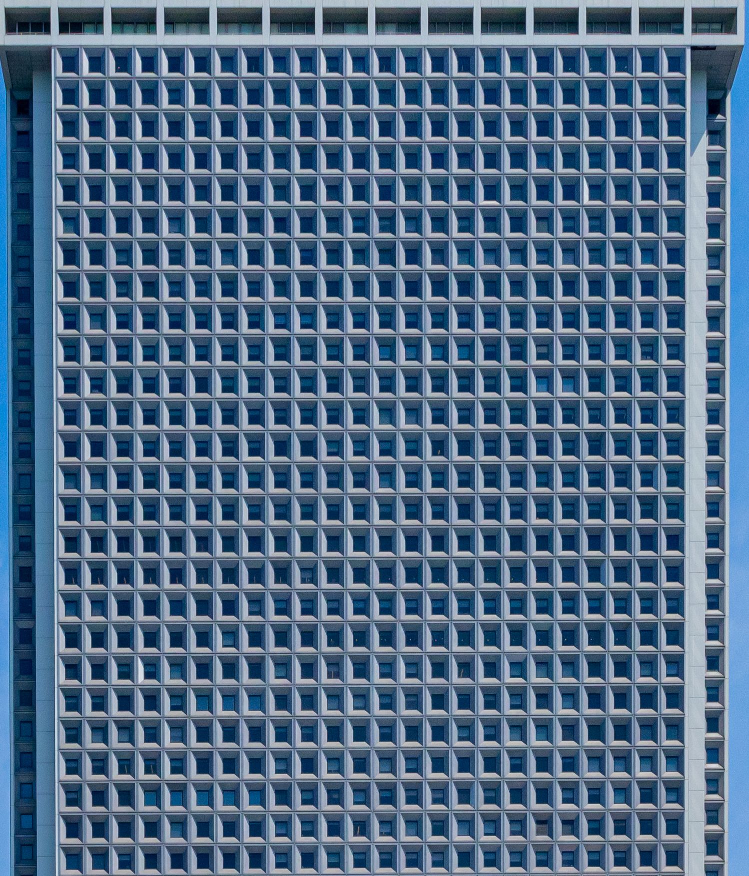 Symmetrical grid pattern of square windows covering the entire facade of a modern blue office skyscraper.