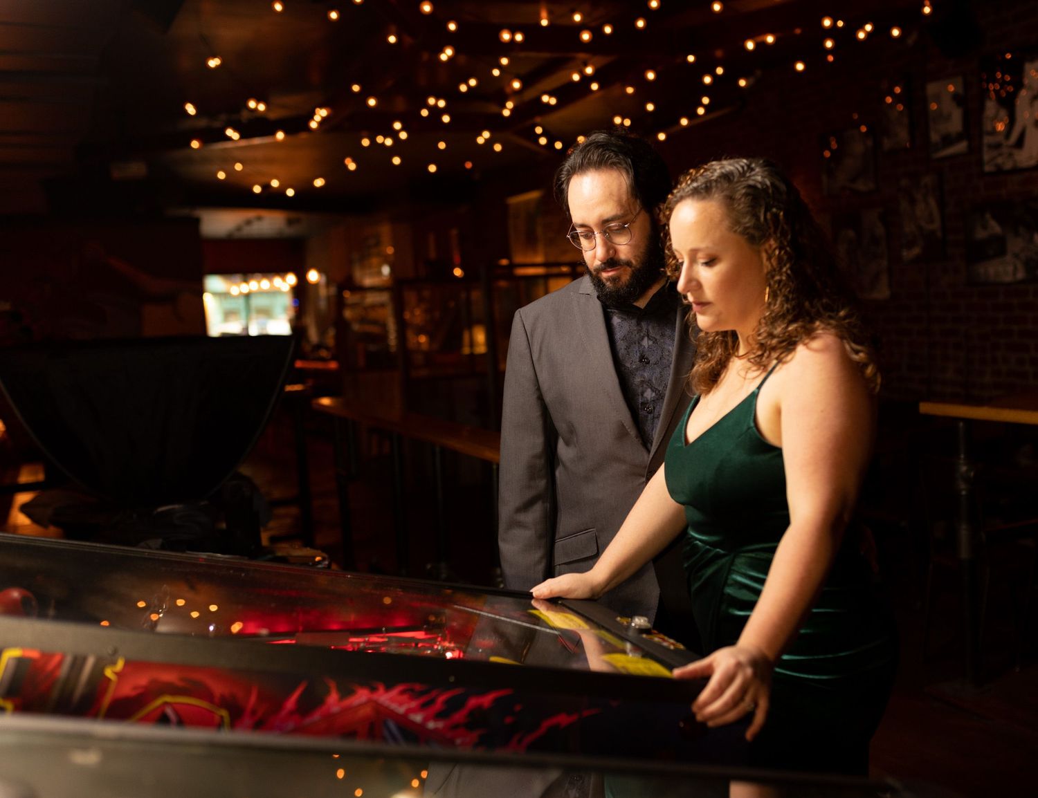 Couple looking at a colorful pinball machine in a dimly lit arcade bar.