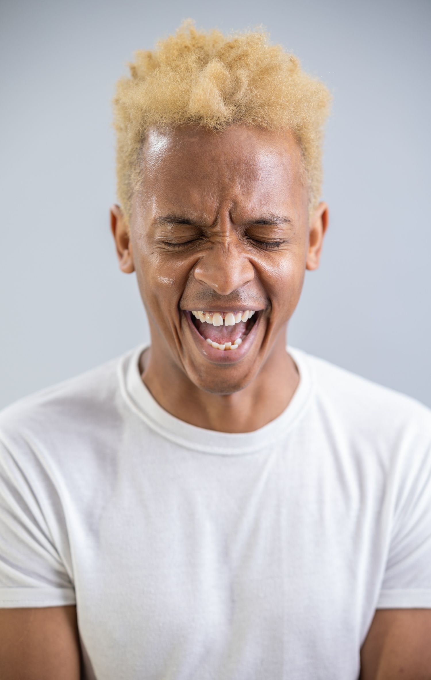 Man with blonde natural hair laughing with eyes closed wearing a white t-shirt.