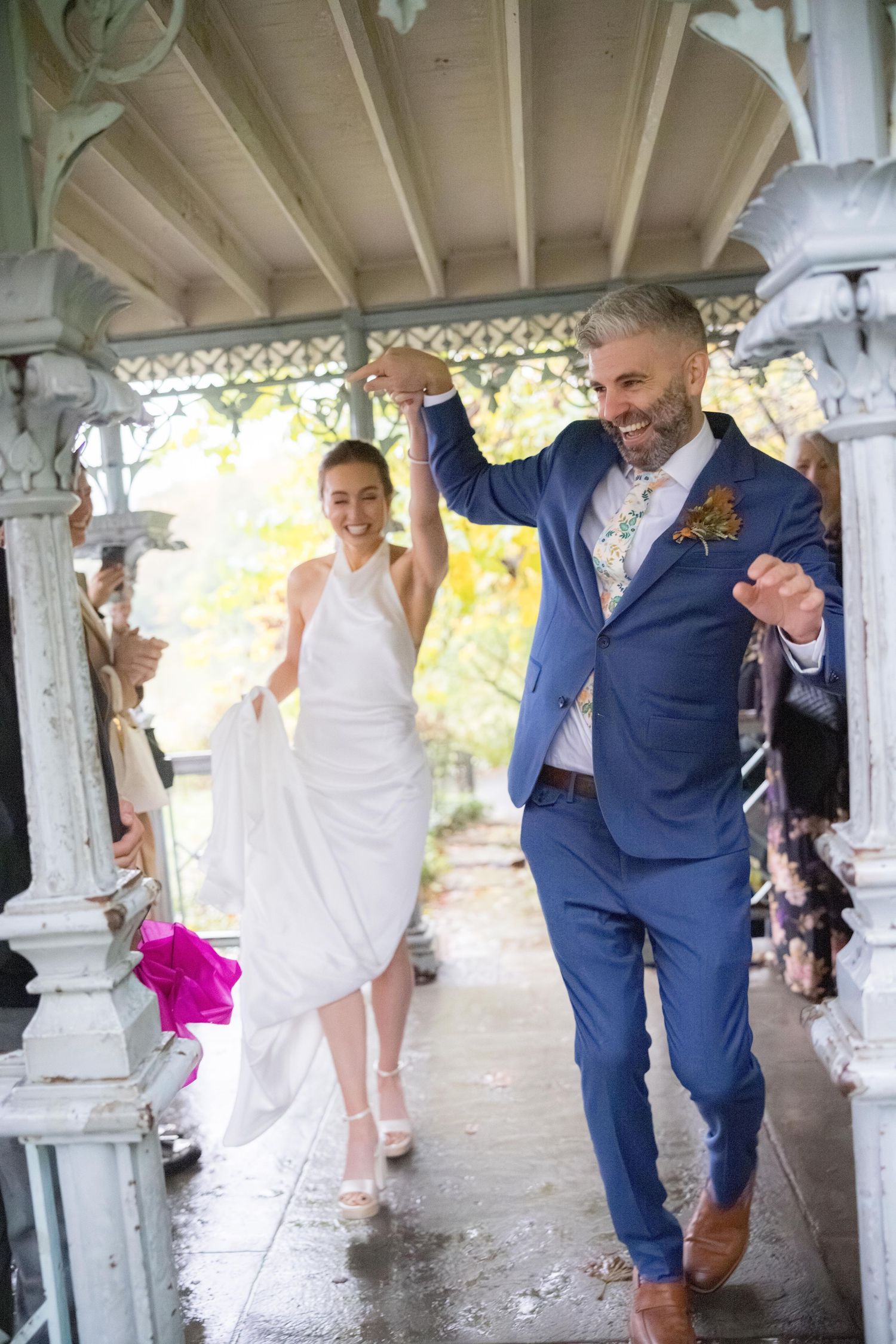Joyful groom in blue suit and bride celebrating their exit from a decorated pavilion.