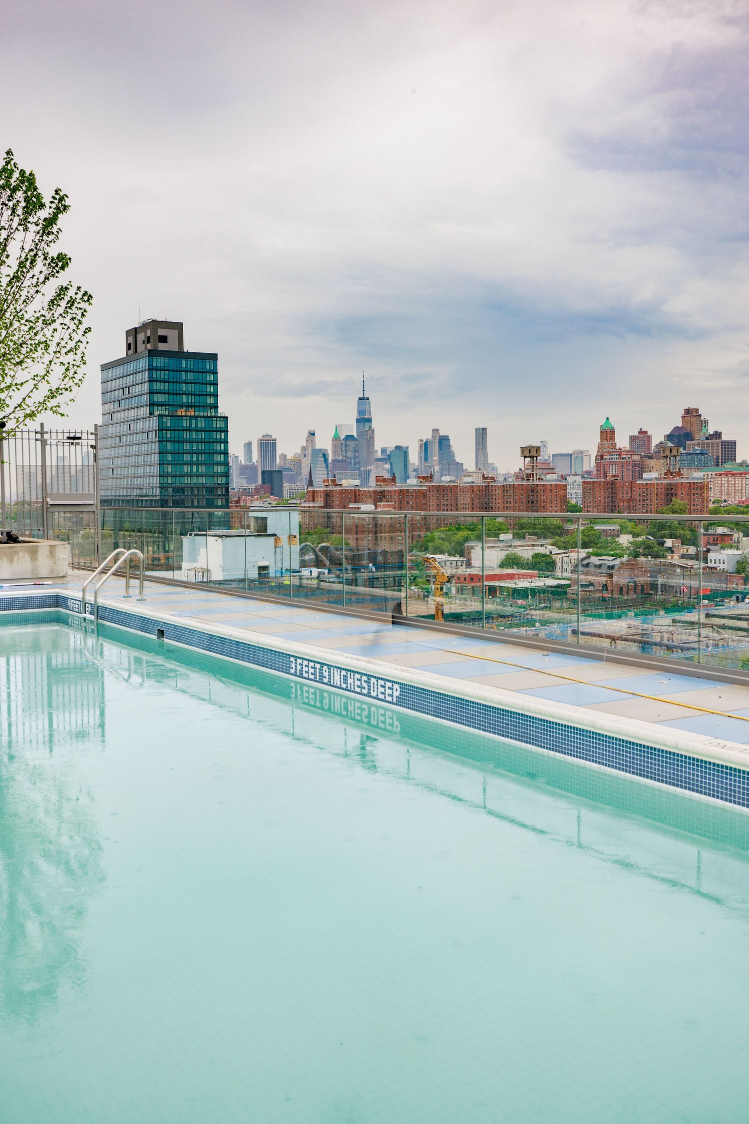 Rooftop pool with stunning New York City skyline views including One World Trade Center on a cloudy day.