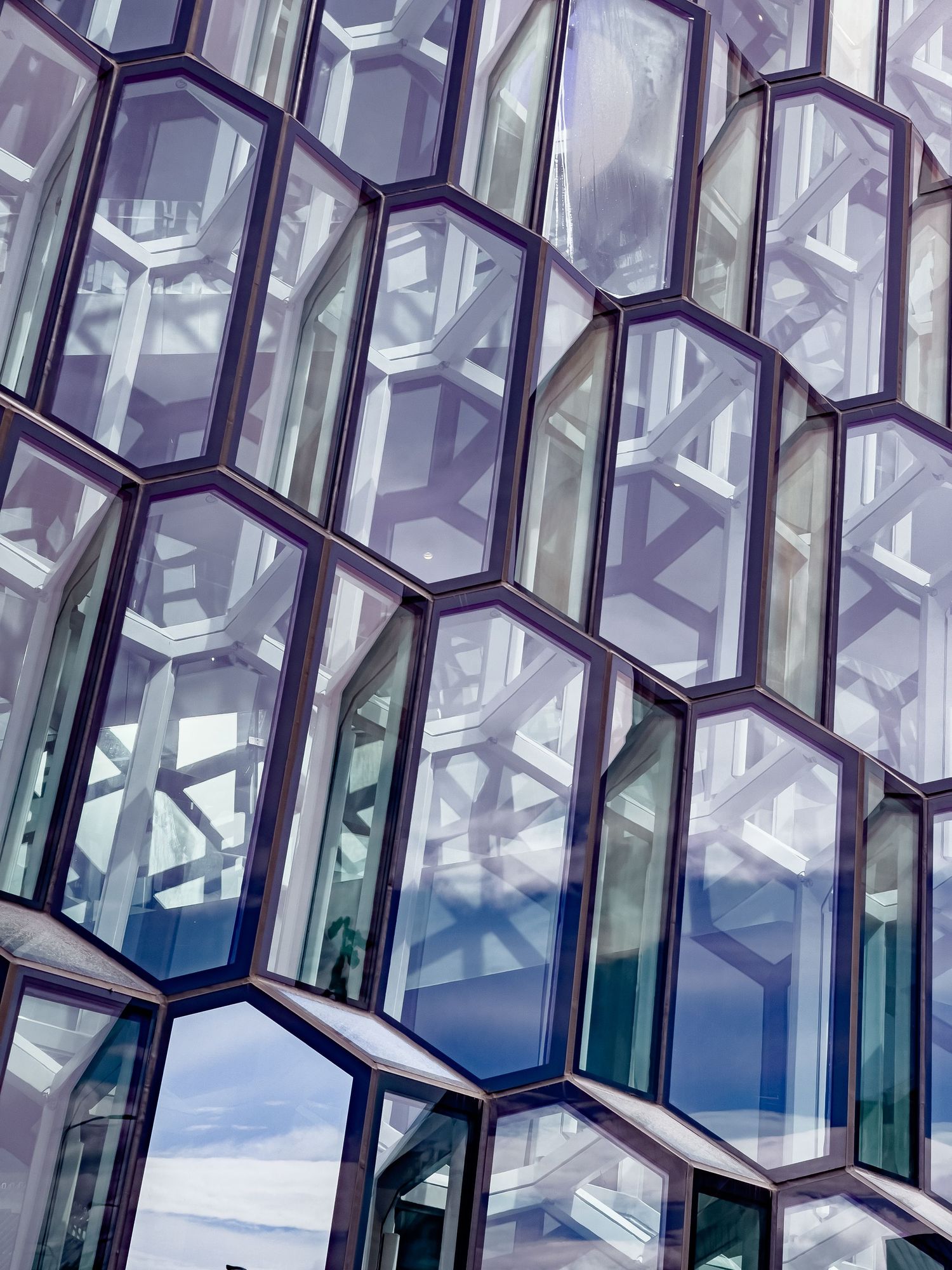 Close-up of geometric honeycomb glass facade reflecting clouds and sky.