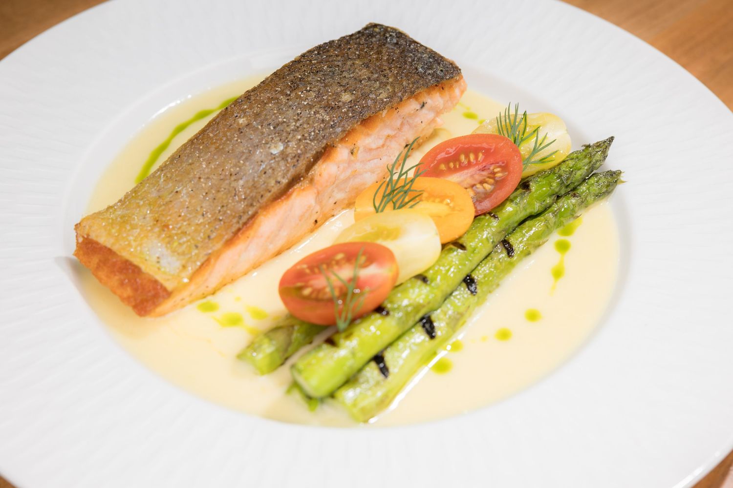 Pan-seared salmon fillet with grilled asparagus, cherry tomatoes, and creamy butter sauce.