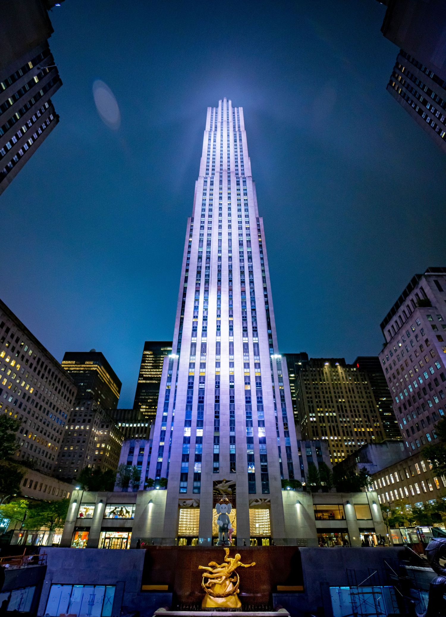 Rockefeller Center illuminated at night with the golden Prometheus statue fountain in the foreground.