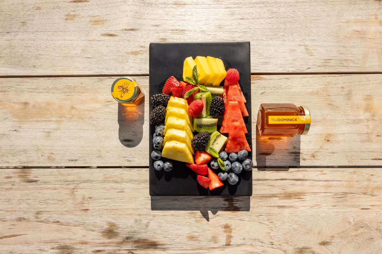Vibrant fresh fruit platter with watermelon, pineapple, berries, and kiwi on a slate board outdoors.