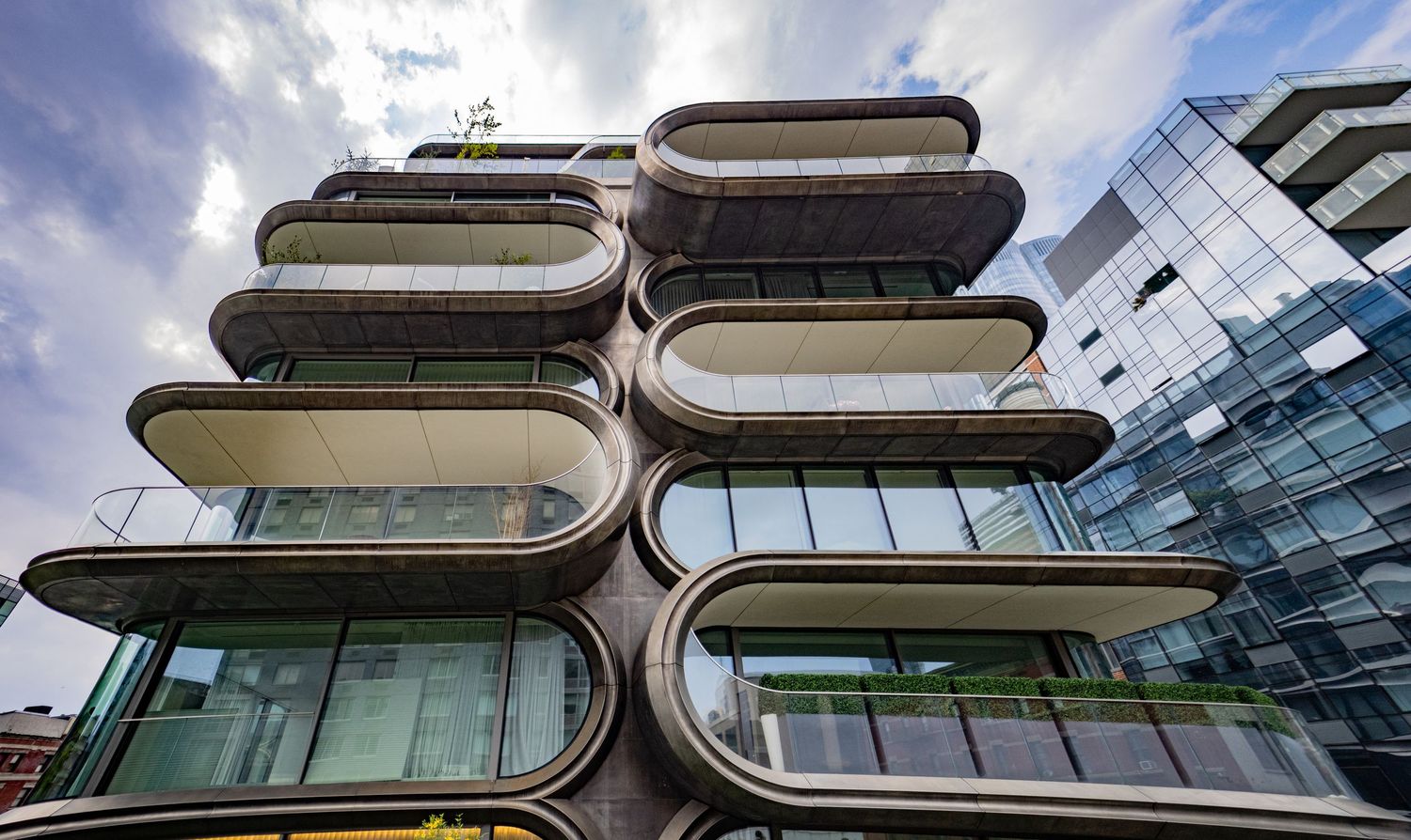 Low-angle view of a contemporary building with curved oval balconies and glass facades against a cloudy sky.