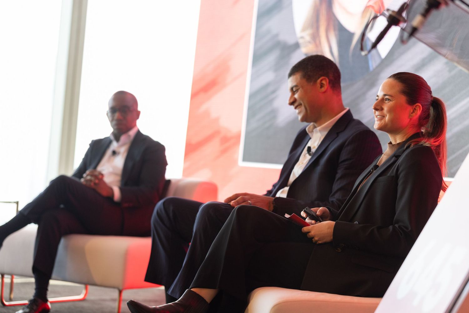 Three professionals engaged in a panel discussion seated on white chairs at a corporate event.