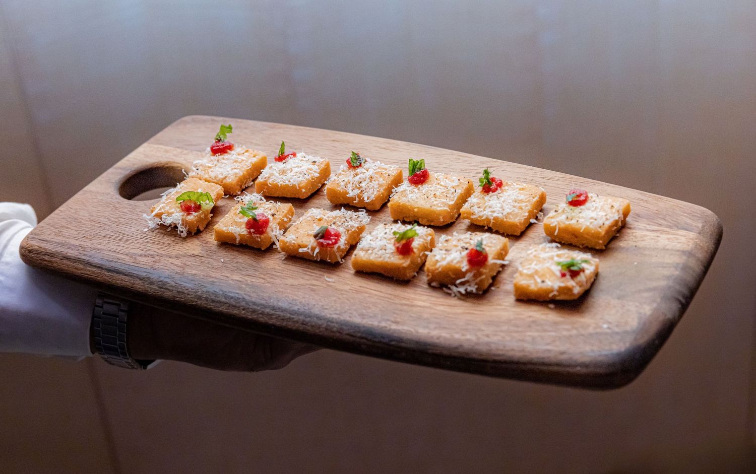 Canapés topped with cheese, pomegranate seeds, and herbs arranged on a rustic wooden cutting board.