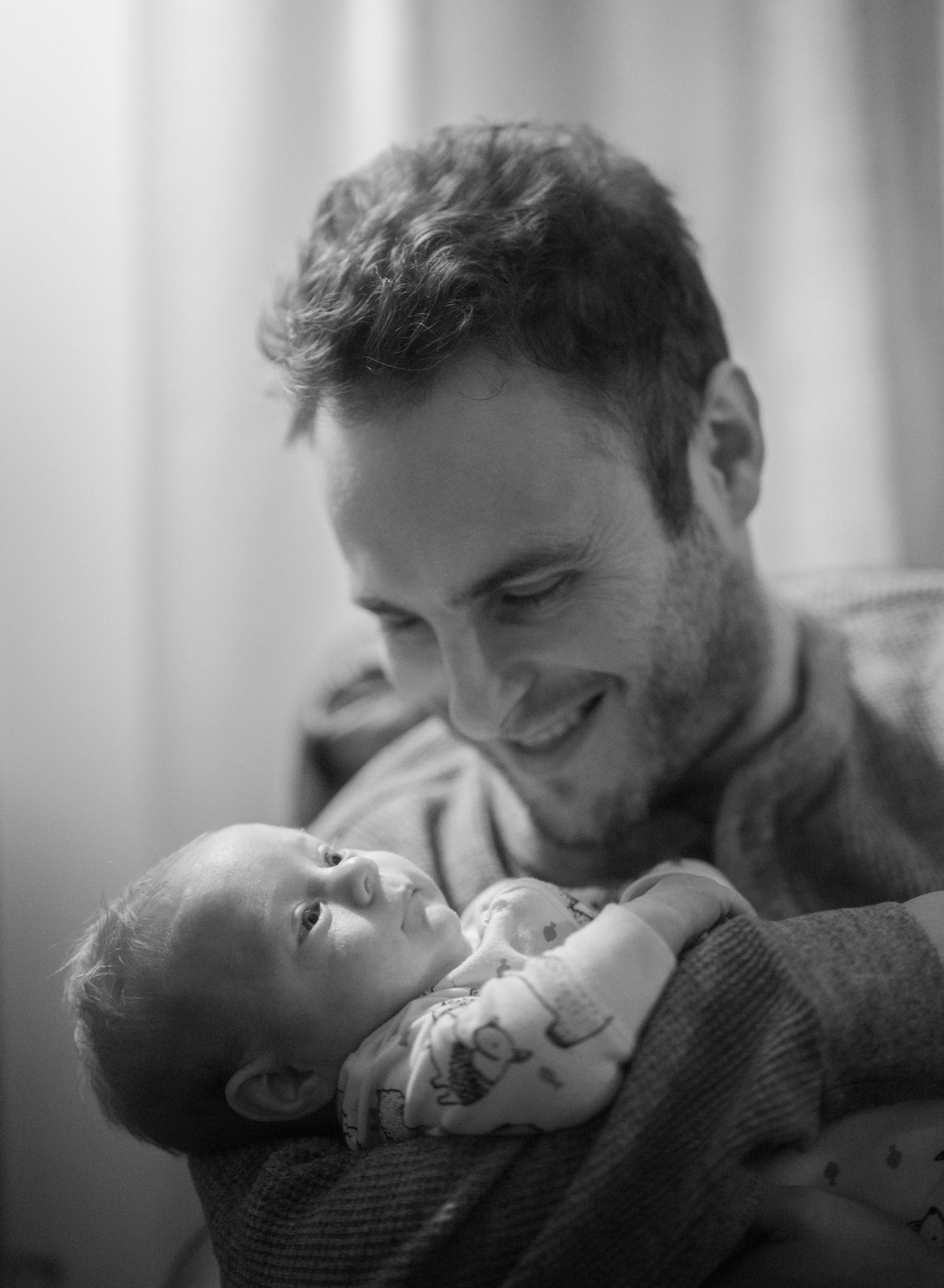 Black and white photo of a smiling man tenderly holding a newborn baby.