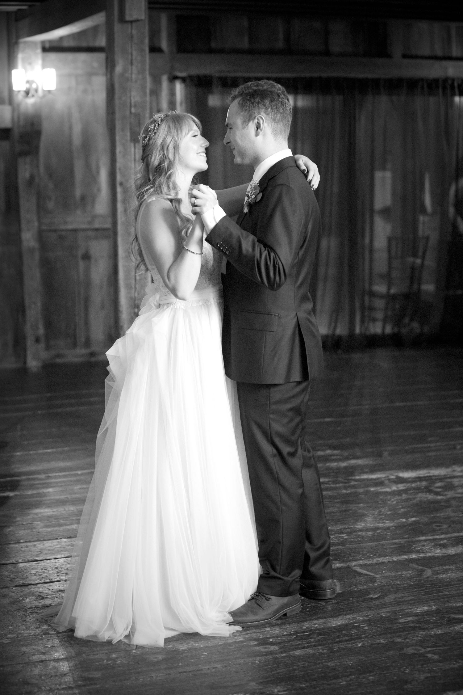 Black and white photo of bride and groom sharing first dance in rustic barn venue.