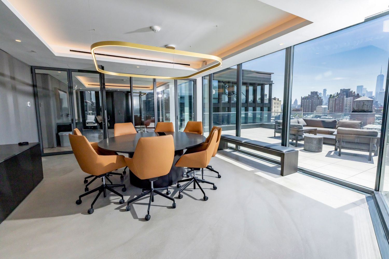 Modern conference room with orange leather chairs around a round table, floor-to-ceiling windows overlooking a city skyline.
