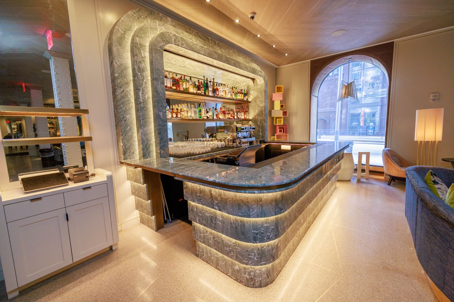 Luxury hotel bar with illuminated marble countertop, curved design, and fully stocked back bar shelving.