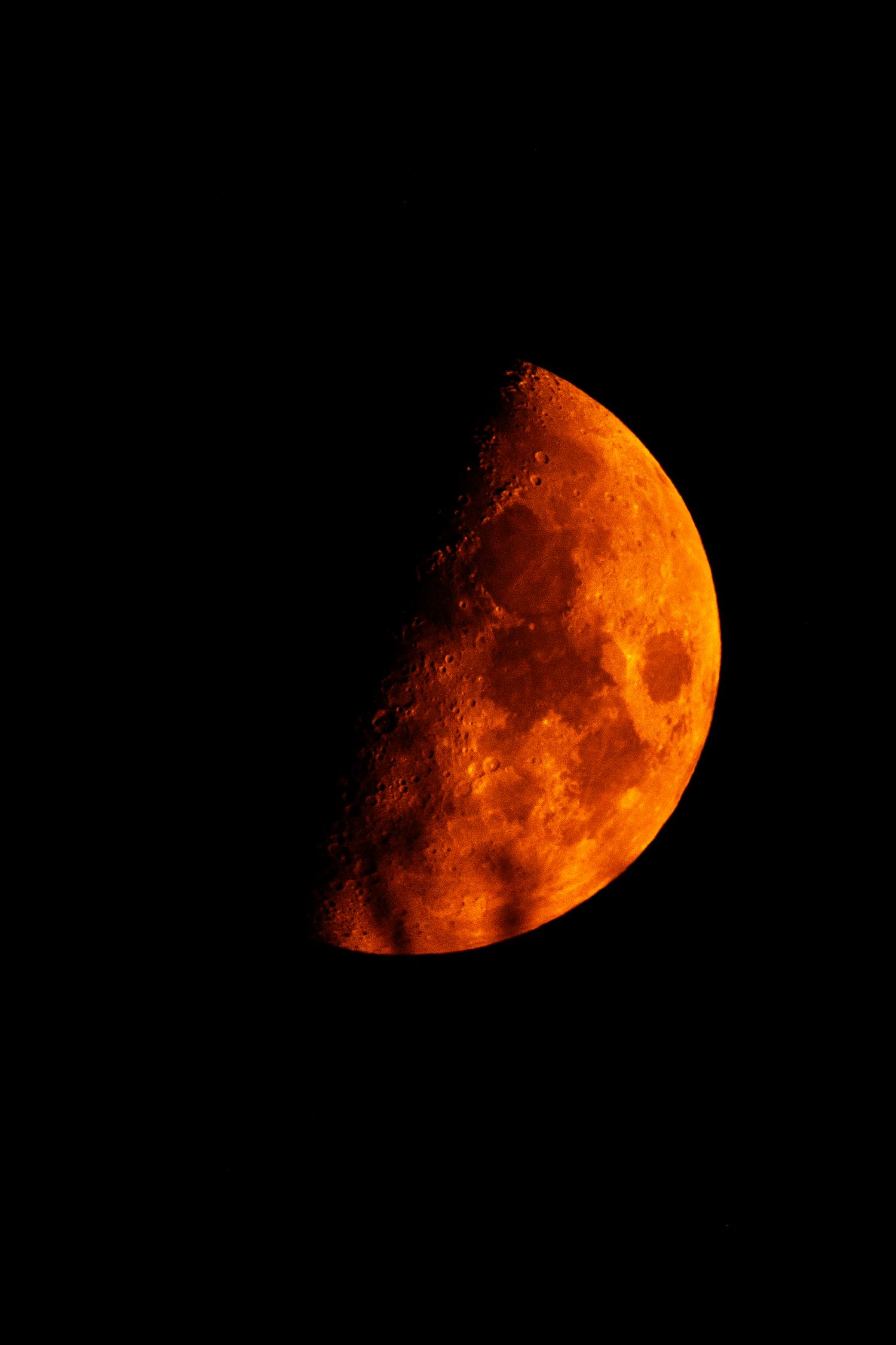 A half moon glowing vivid orange-red against a dark black night sky.