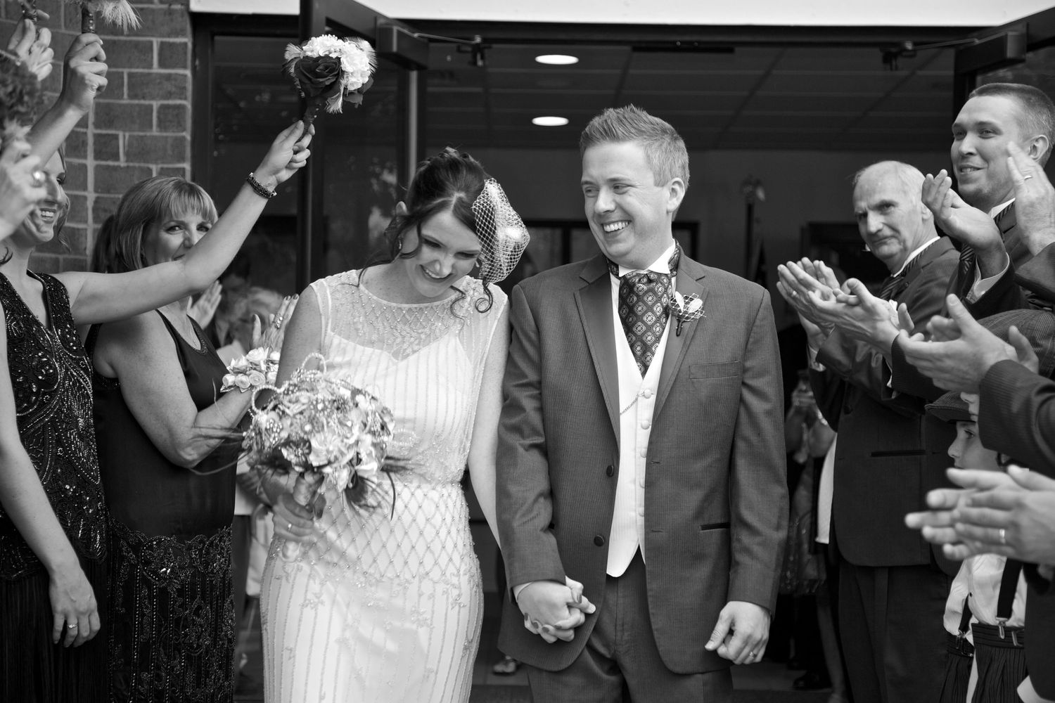 Smiling newlyweds walking through cheering guests after their wedding ceremony in black and white.