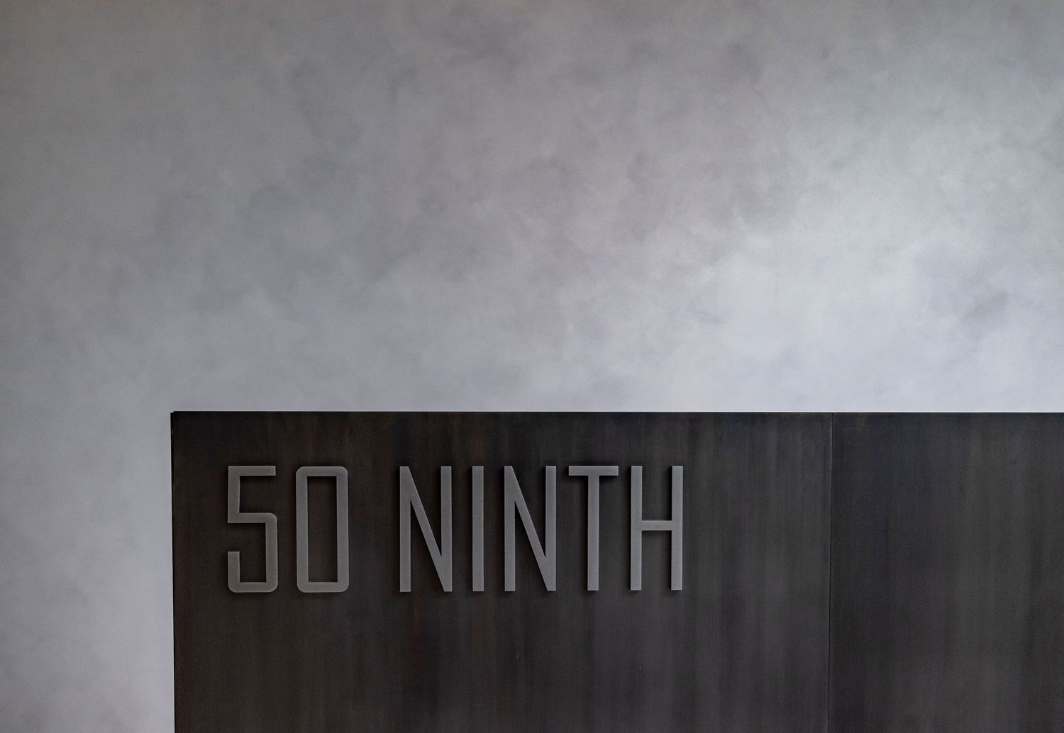 Modern dark wood reception desk with embossed 50 Ninth signage against a textured gray concrete wall.