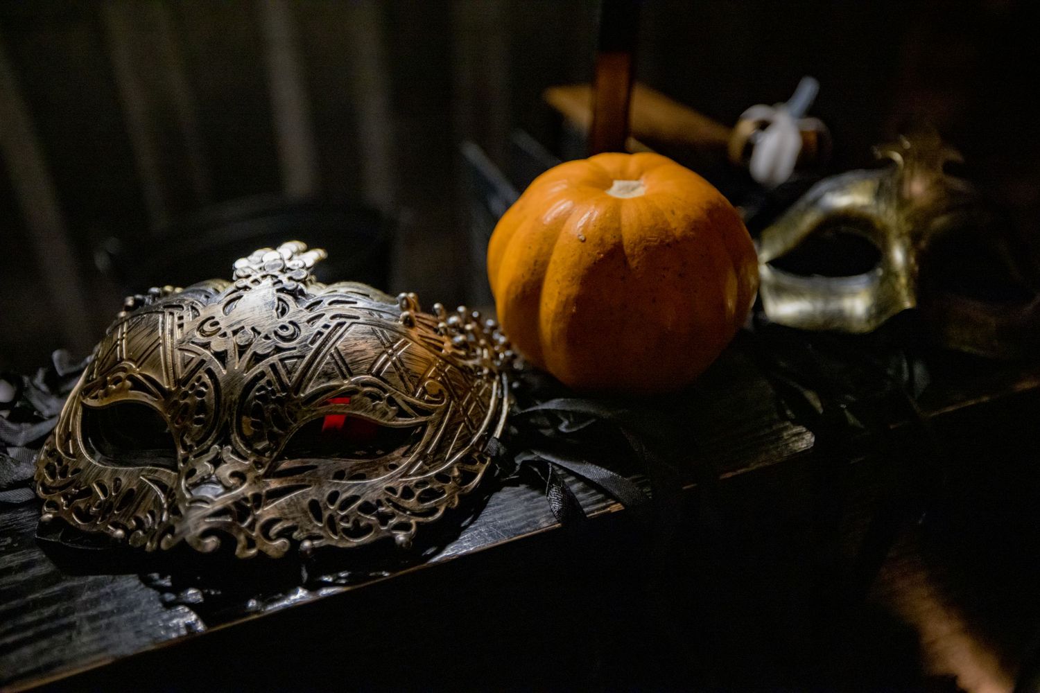 Ornate masquerade masks and orange pumpkin arranged on dark surface for Halloween.