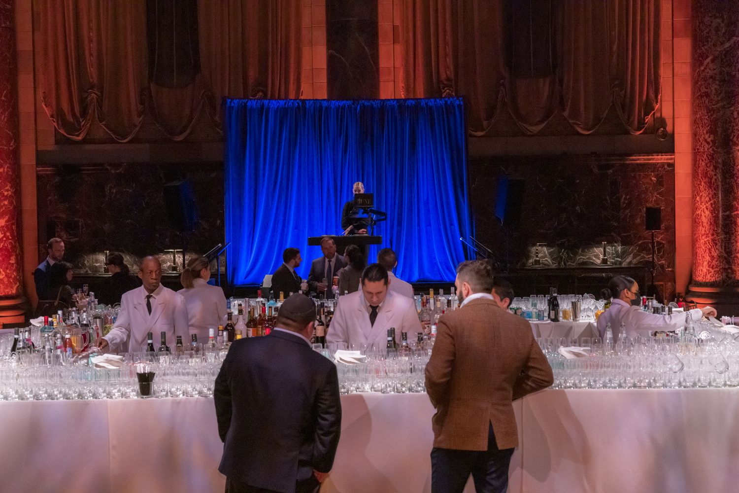 Bartenders serving guests at an elegantly lit event bar with blue stage backdrop.