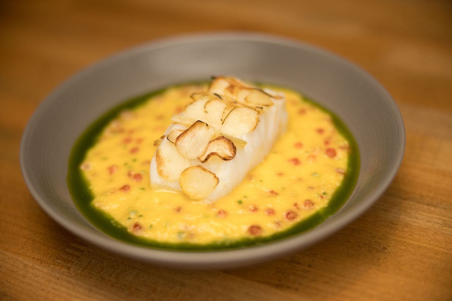 Perfectly cooked white fish fillet in golden saffron broth with green herb oil swirl.