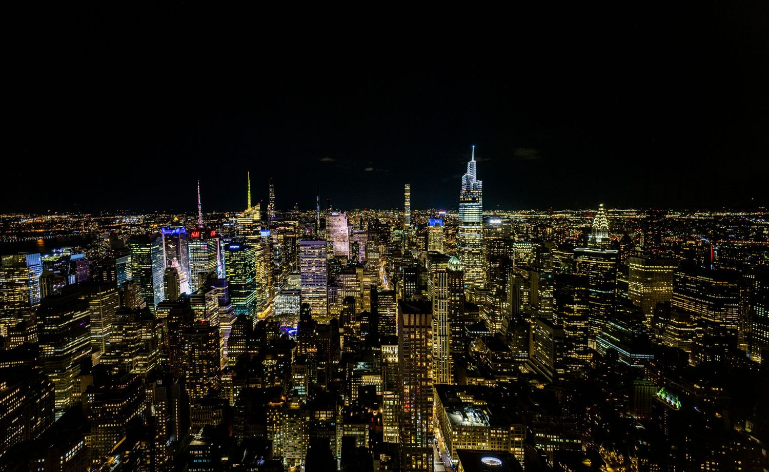 An aerial panoramic view of New York City skyline illuminated brilliantly at night with thousands of glittering lights.