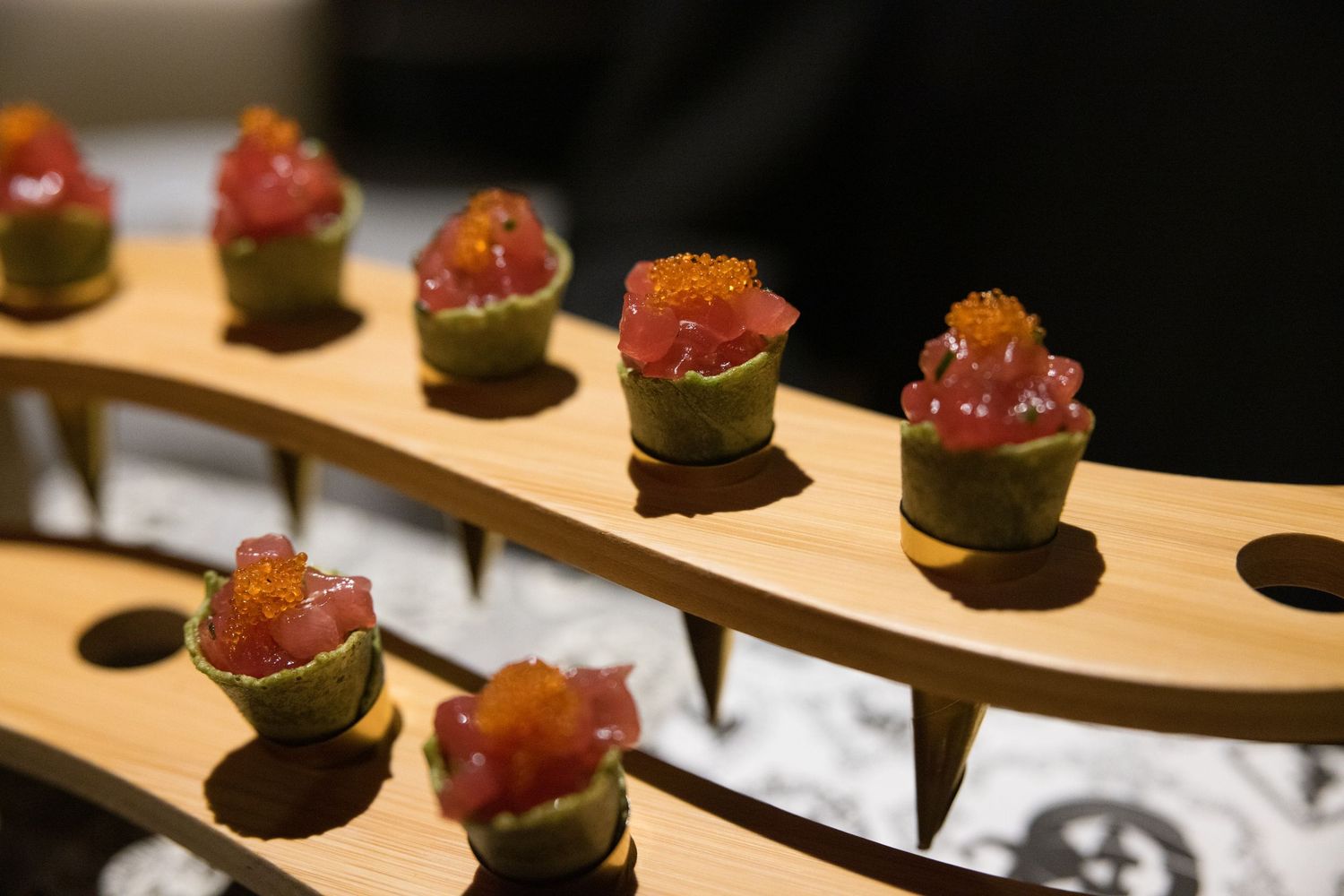 Elegant tuna tartare appetizers topped with tobiko served in green avocado cups on a wooden board.