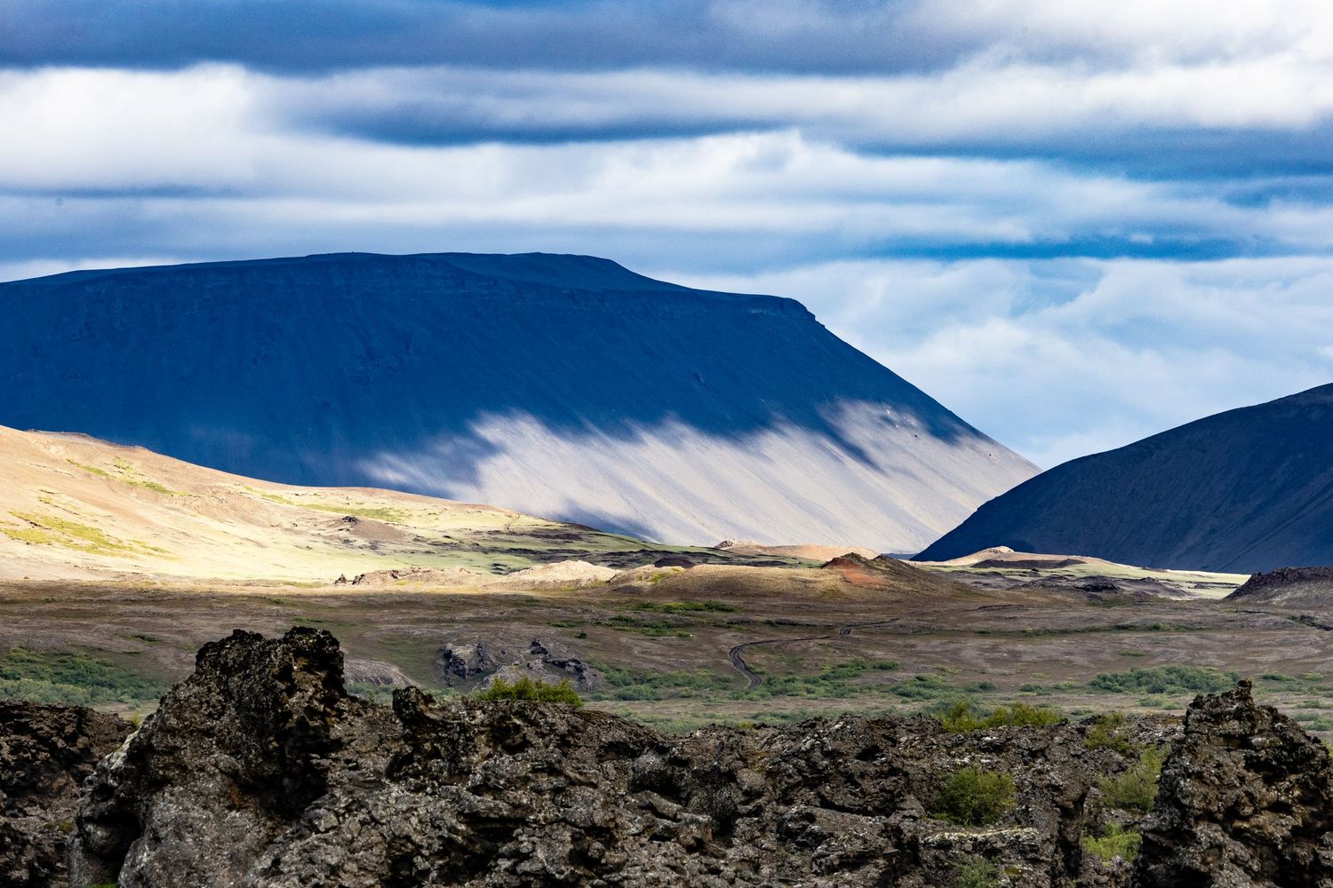 Dramatic Icelandic volcanic landscape with rugged lava fields and sunlit mountain slopes under cloudy skies.