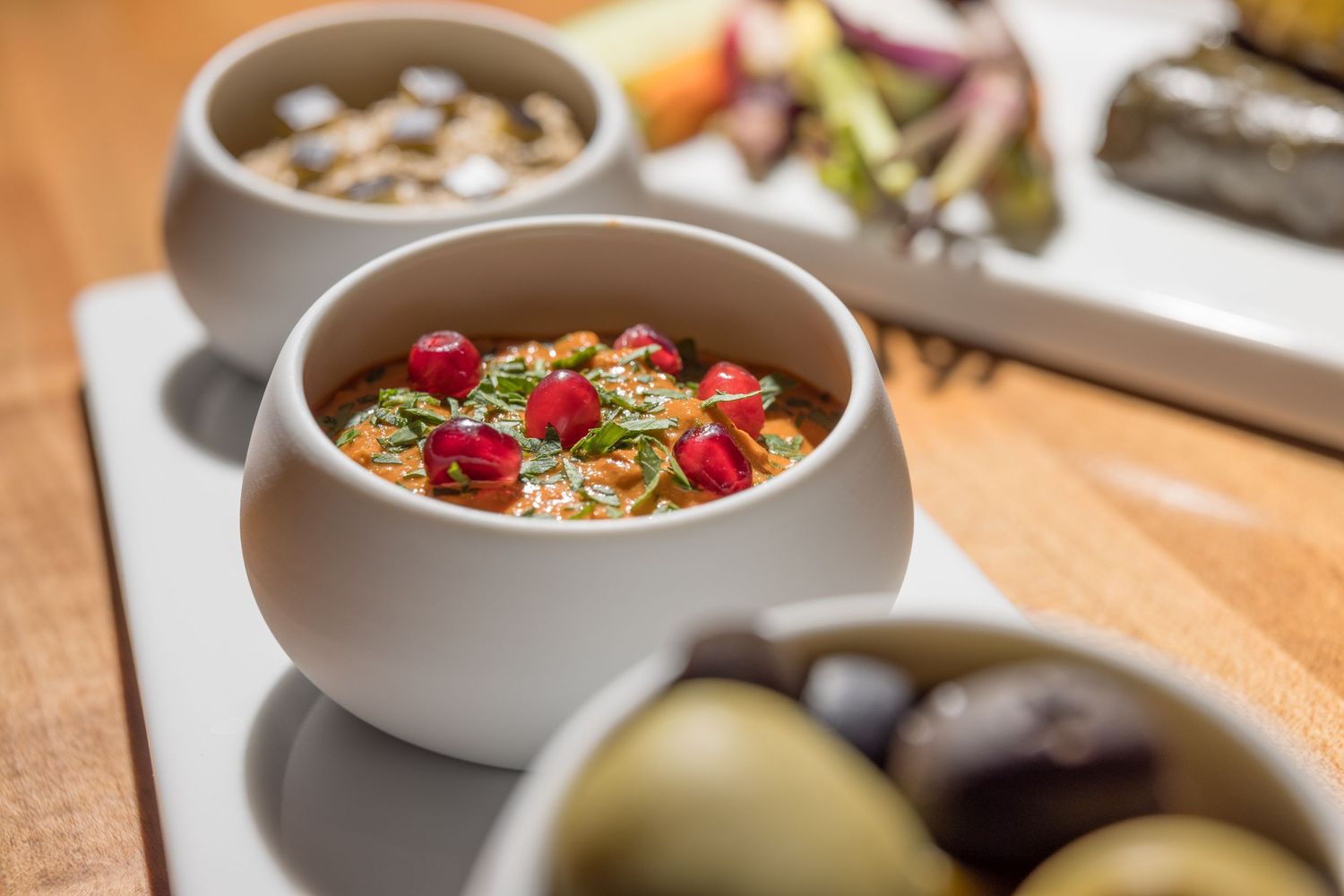 Gourmet appetizer spread featuring marinated vegetables in white ceramic bowls with olives on a platter.