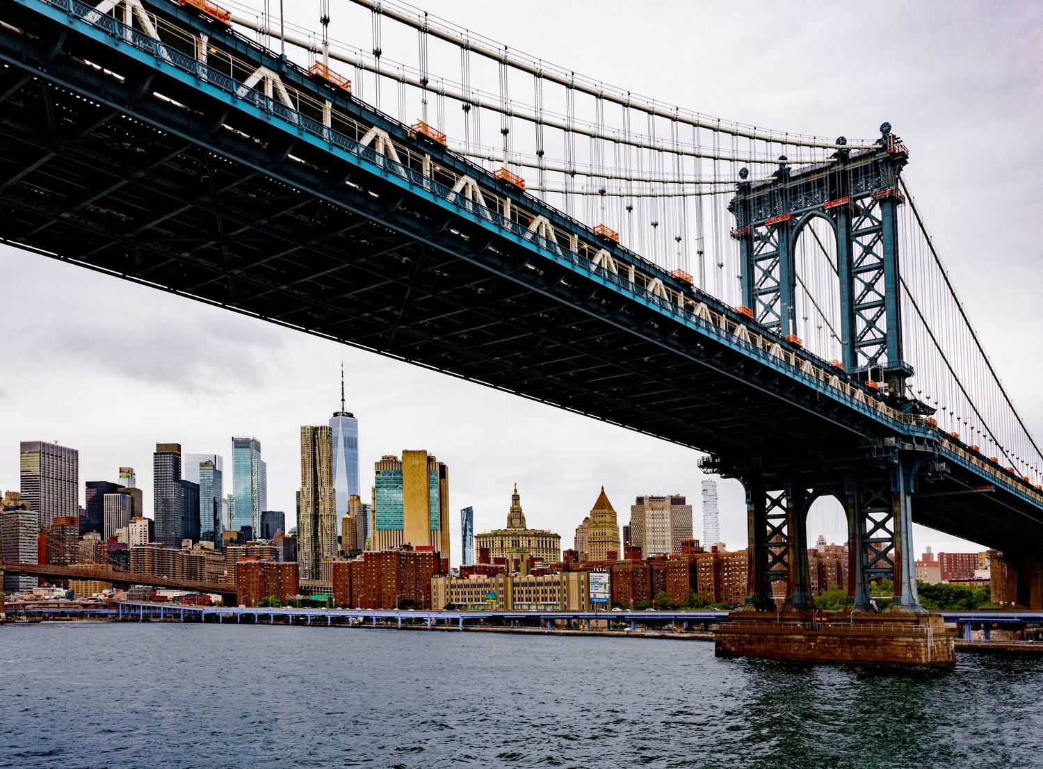 Manhattan Bridge spanning the East River with NYC skyline and One World Trade Center visible in the background.