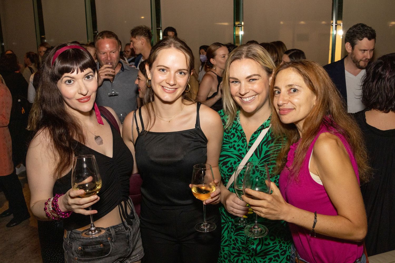 Four white women smiling and holding wine glasses at an elegant indoor social event.