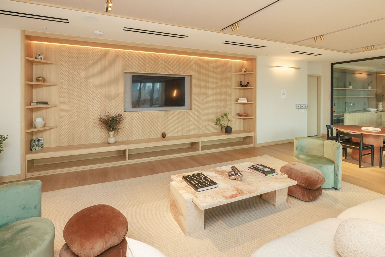 Contemporary living room featuring built-in wood shelving, wall-mounted TV, and colorful velvet accent chairs.